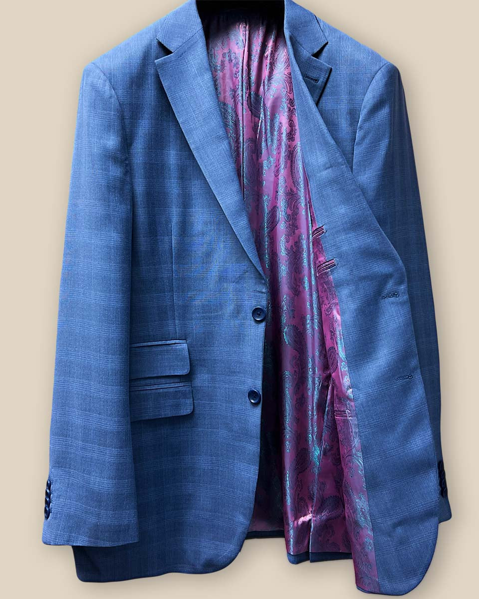 The inside left view of a medium blue Prince of Wales glen plaid suit jacket, showcasing the pink and purple iridescent paisley lining.