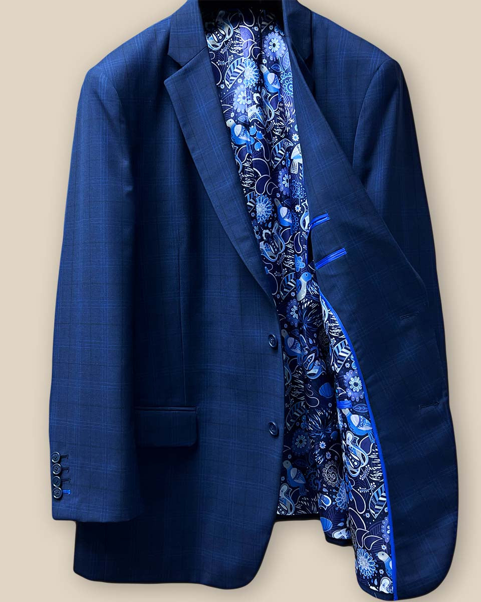 Interior view of the left side of the dark blue windowpane men's sport coat showcasing the blue and white aviary motif flash lining and royal blue piping.