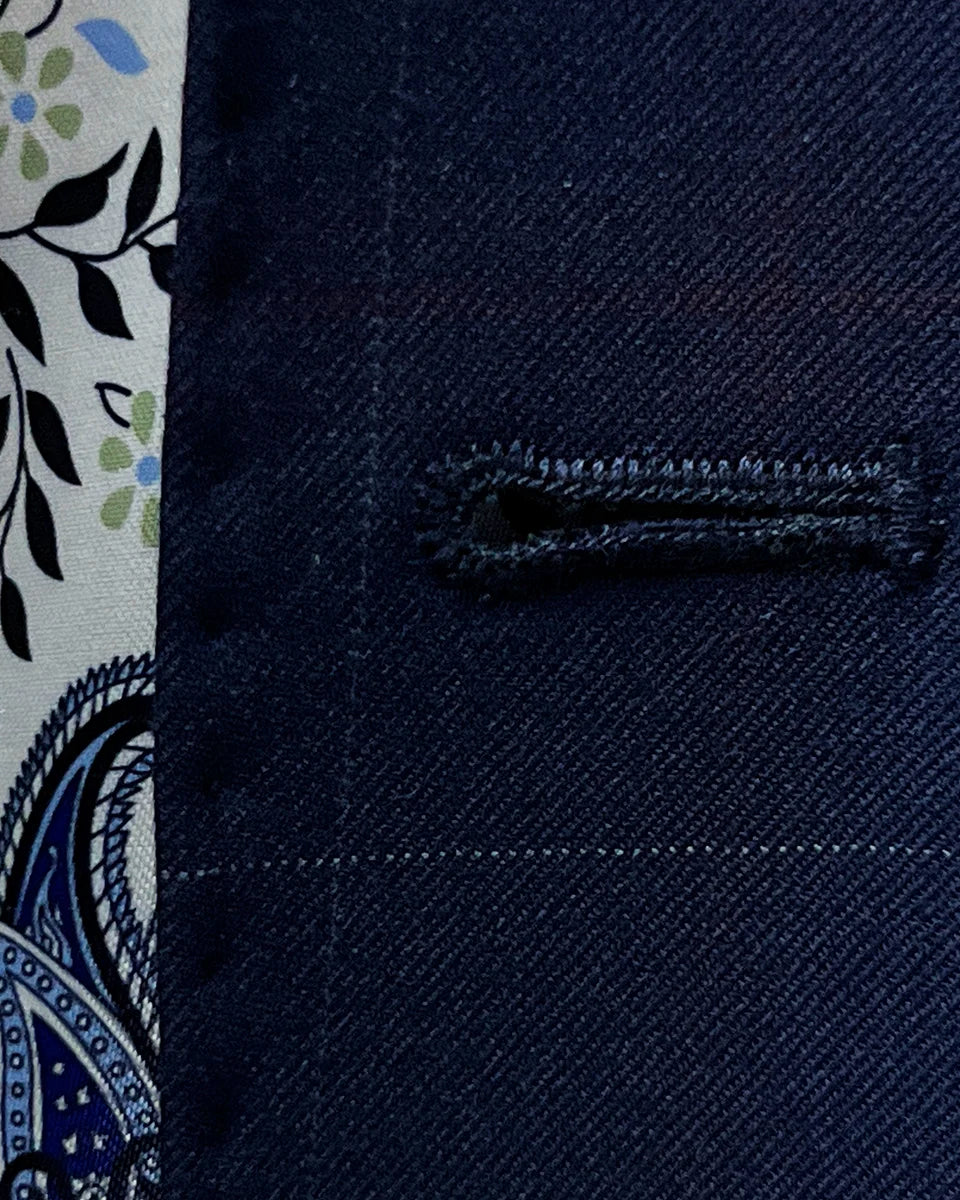 Macro view of the precise white contrast buttonhole stitching showing the quality handwork on the navy wool fabric