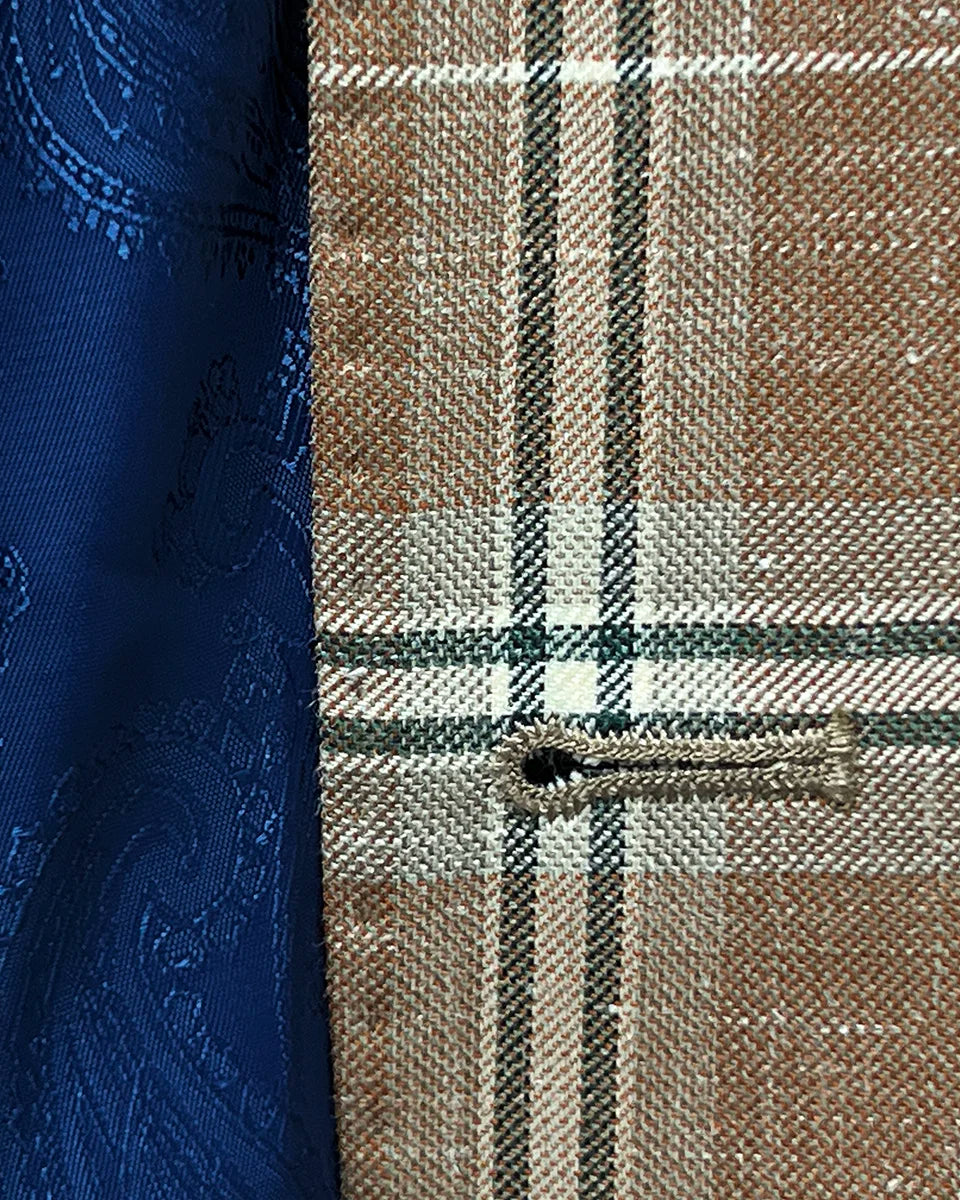 Close up view of buttonhole craftsmanship on a brown beige men's sport coat with blanched almond and midnight blue windowpane pattern.