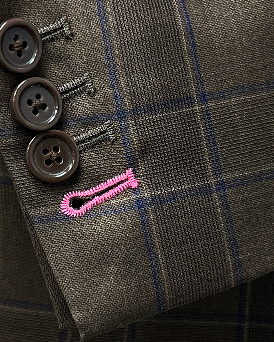 Close-up view of the contrast pink accent buttonholes on a chocolate brown sportcoat.