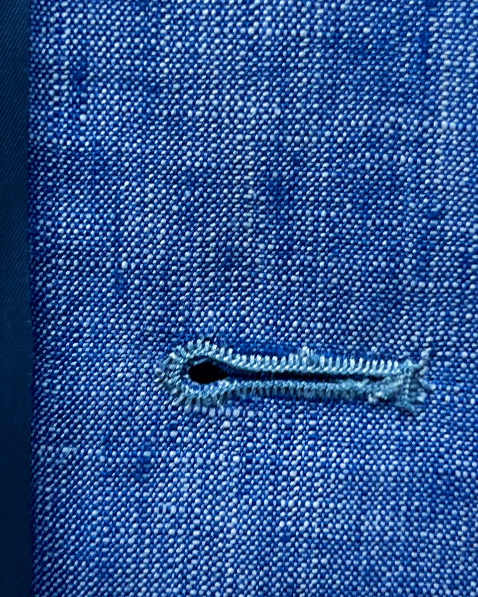 Macro shot of buttonhole stitching on light blue solid Irish linen men's suit, highlighting quality craftsmanship