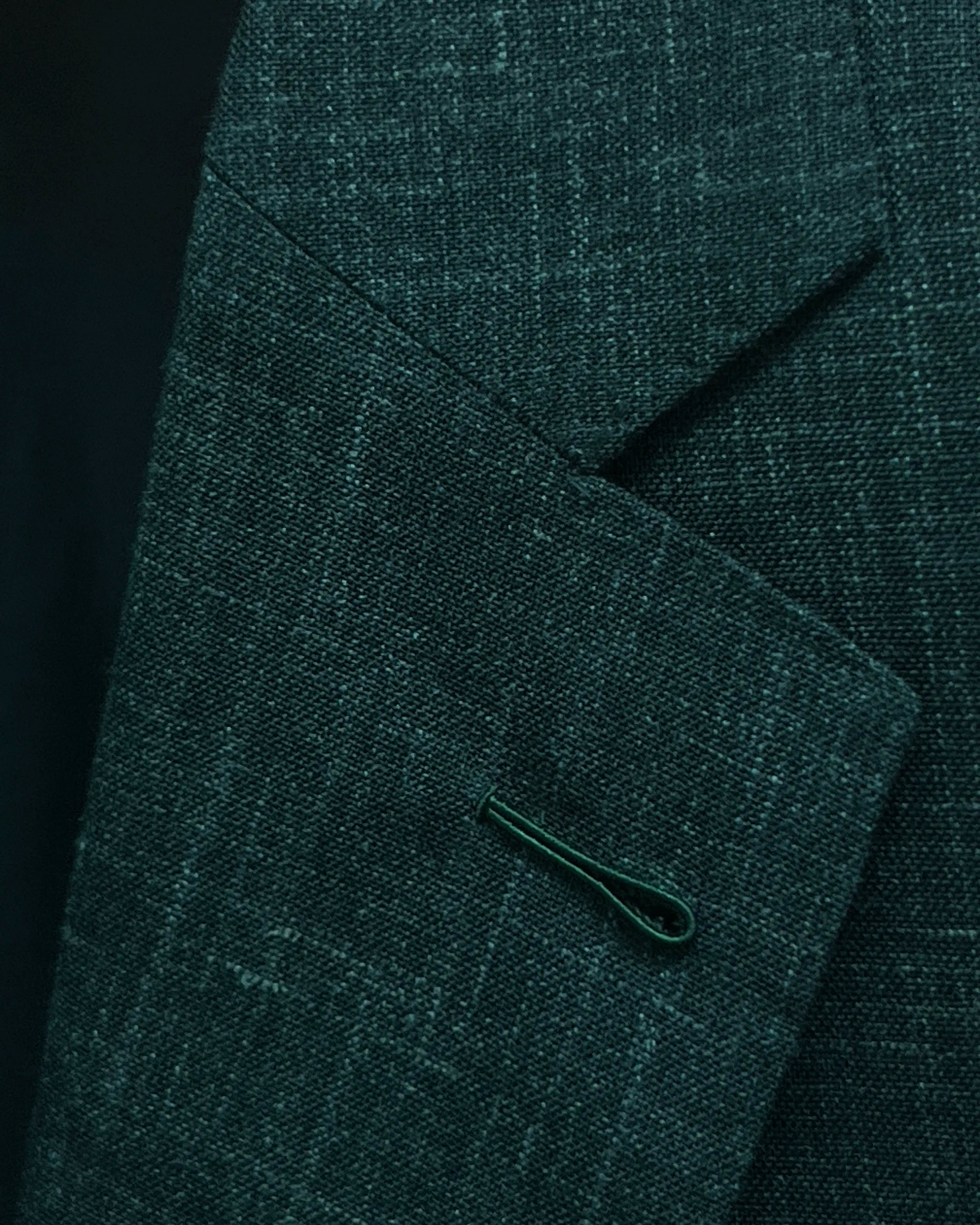 Lapel buttonhole detail image of deep green solid men's suit showing standard Milanese lapel buttonhole with no contrast thread