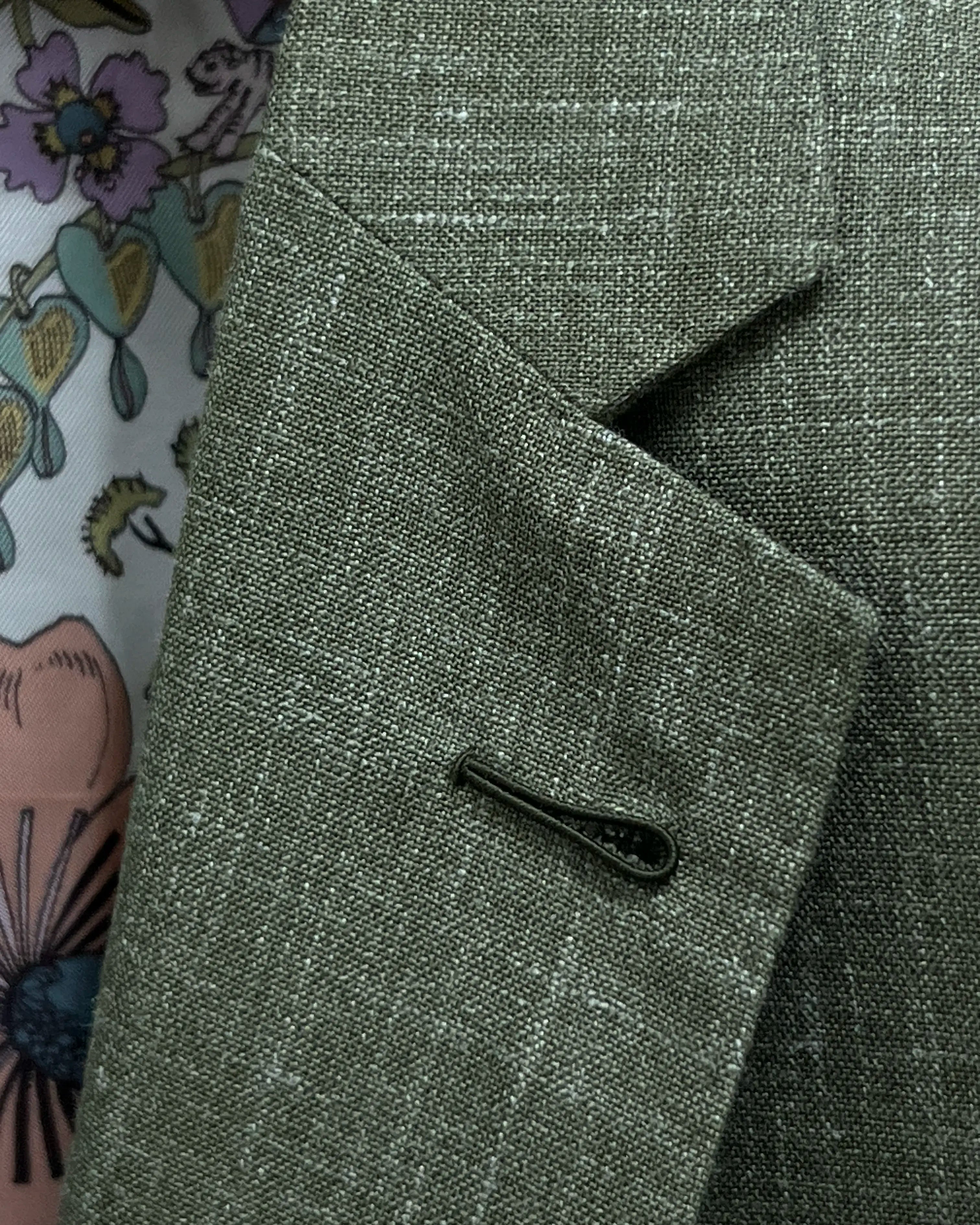 Macro close-up of Milanese lapel buttonhole on sage green plain men's suit showing raised cord detail