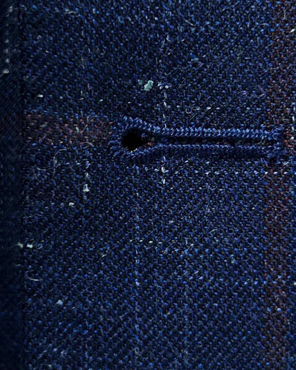 Macro view of hand-picked buttonhole stitching detail showing ruby red contrast thread work on navy windowpane fabric