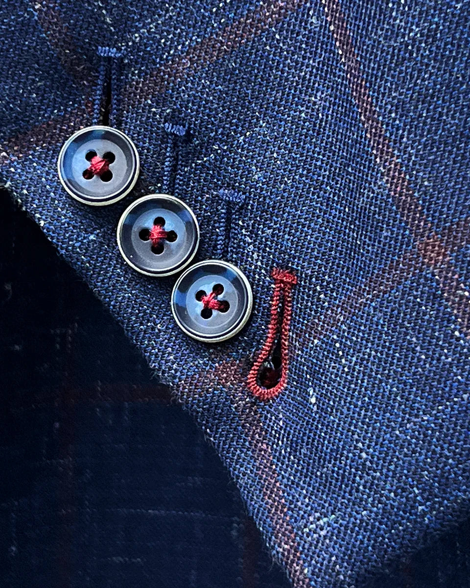 Close-up of functional slanted sleeve buttonholes with ruby red contrast stitching on navy windowpane sport coat cuff
