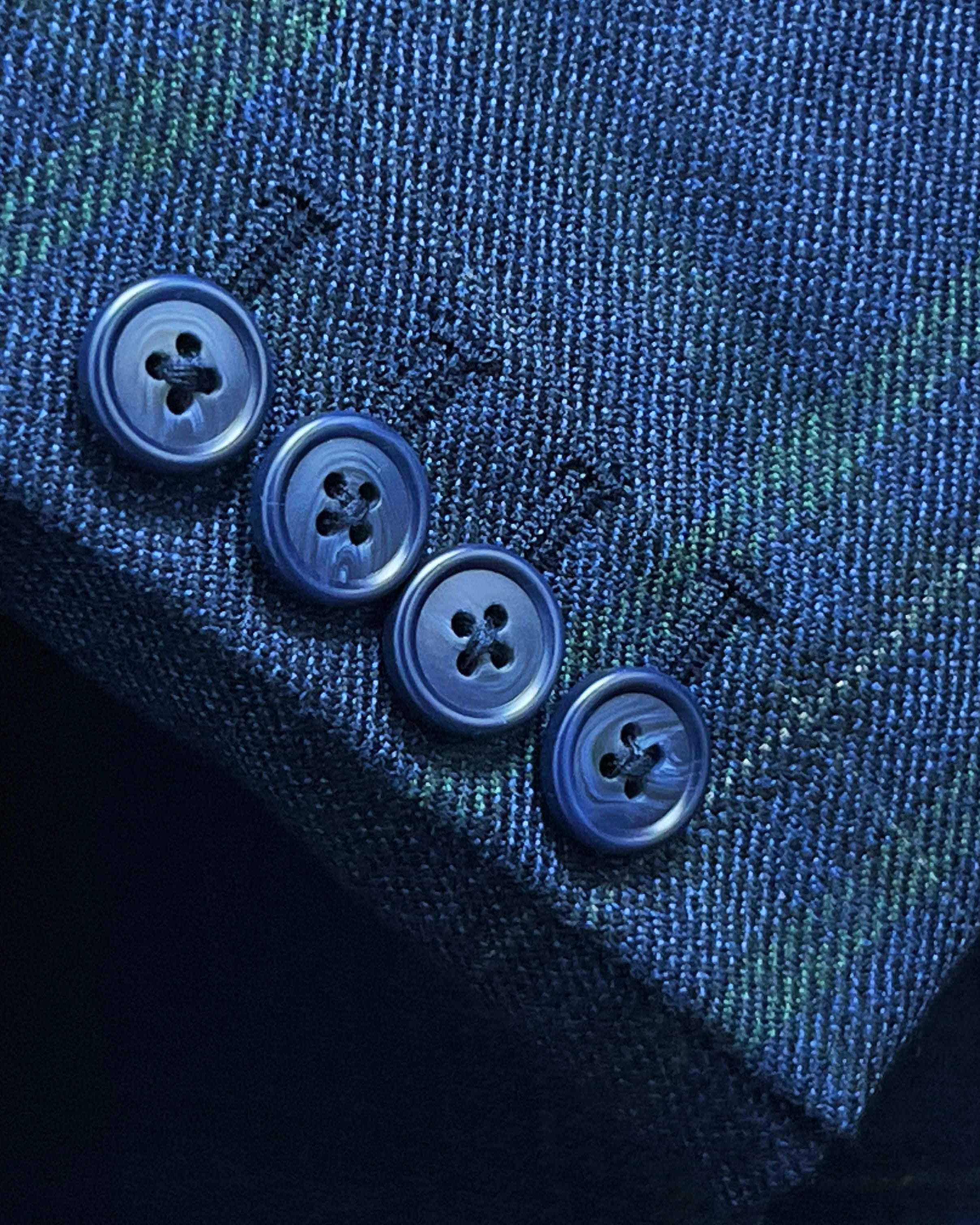 Suit jacket sleeve cuff showing functional buttonholes with contrast navy accent stitching on deep blue overcheck fabric