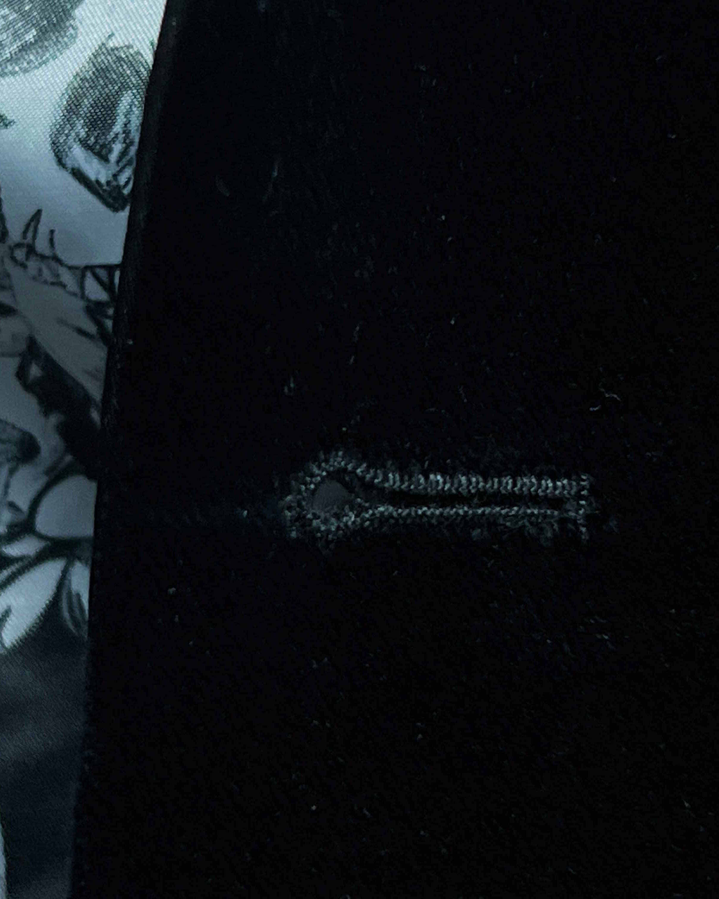 Detailed macro shot of hand-finished buttonhole stitching on black silk velvet formalwear tuxedo with contrast thread