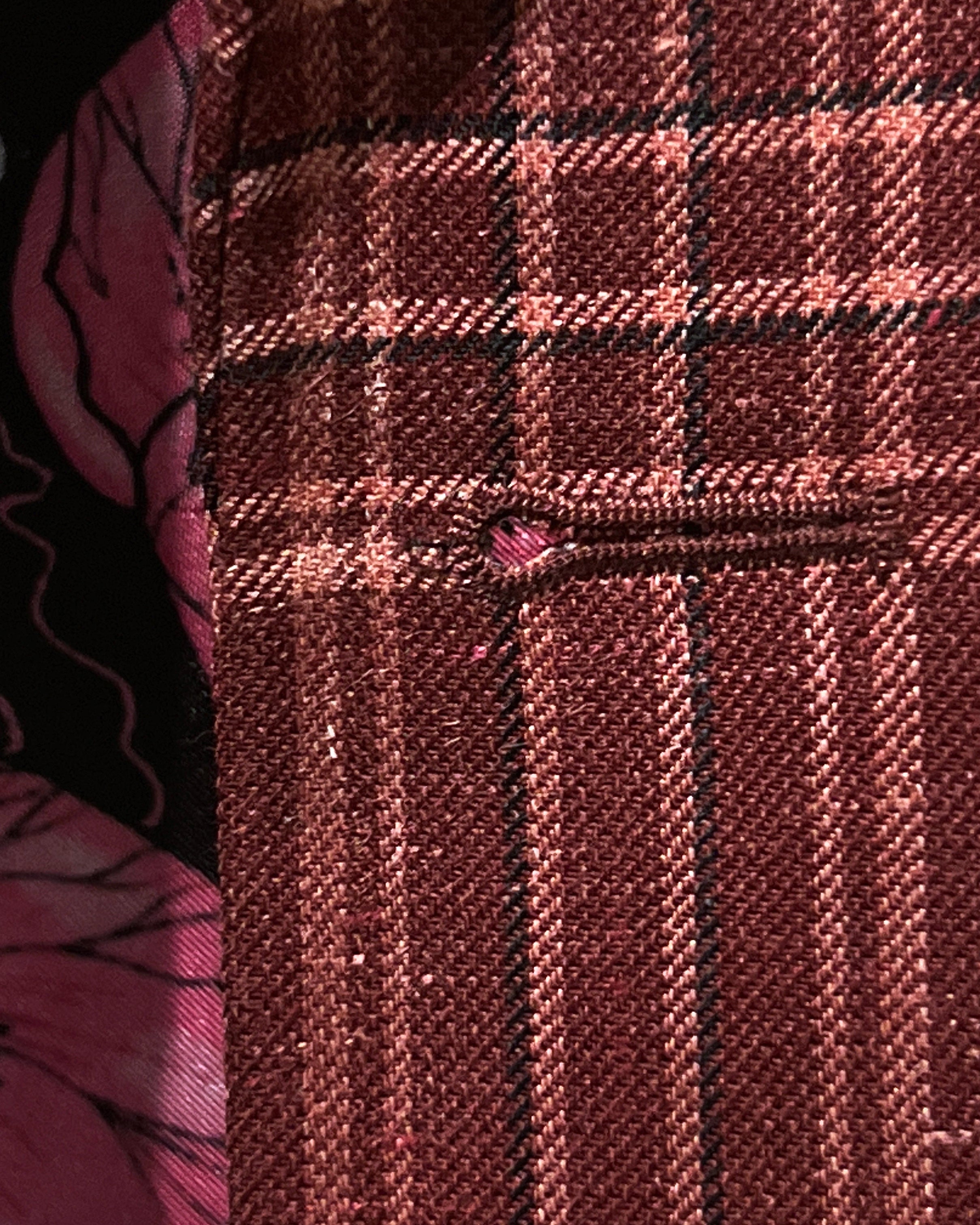 Detailed macro shot of hand-finished buttonhole stitching on burgundy plaid sport coat with white contrast thread