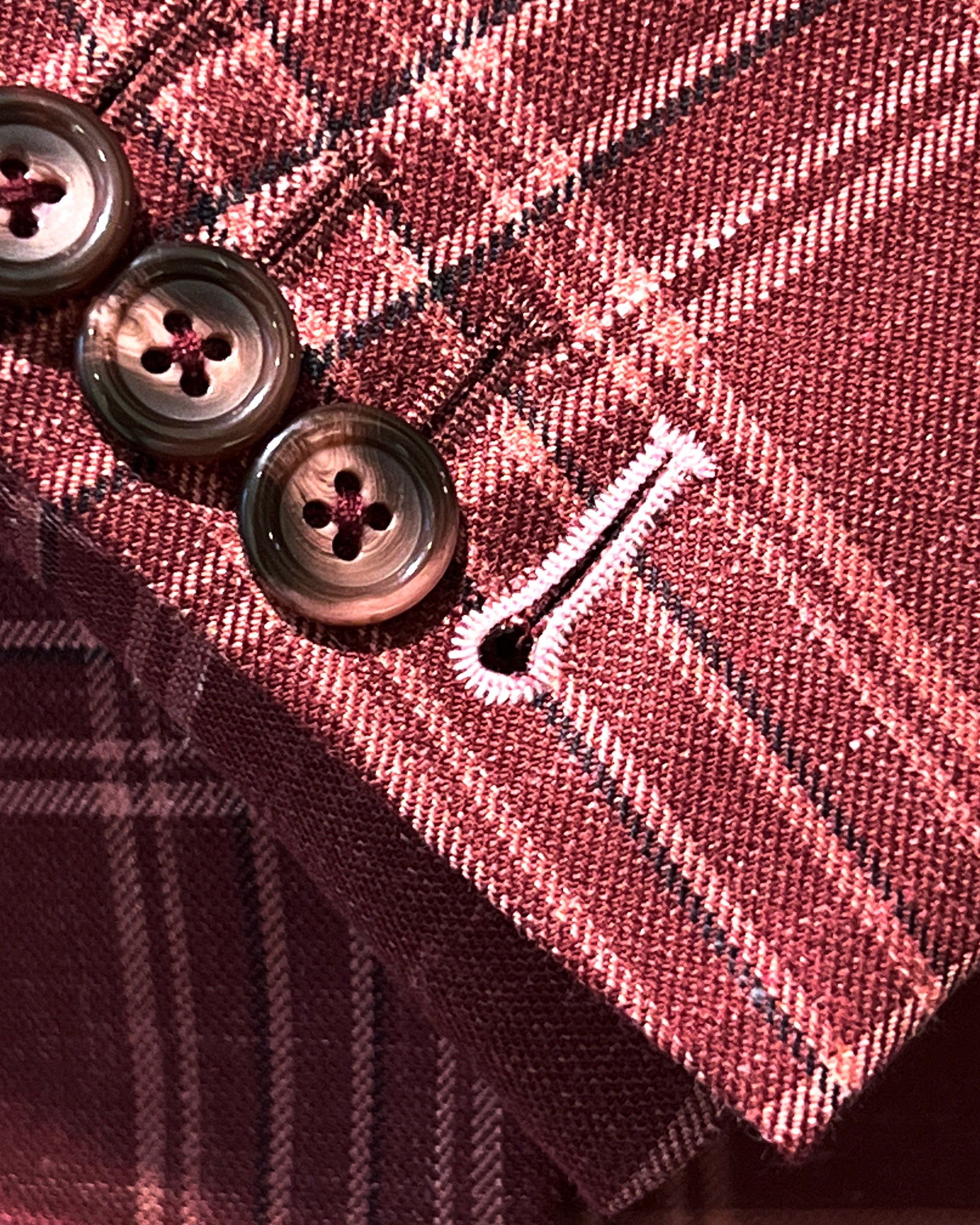 Sport coat sleeve cuff showing functional buttonholes with contrast white accent stitching on burgundy plaid fabric