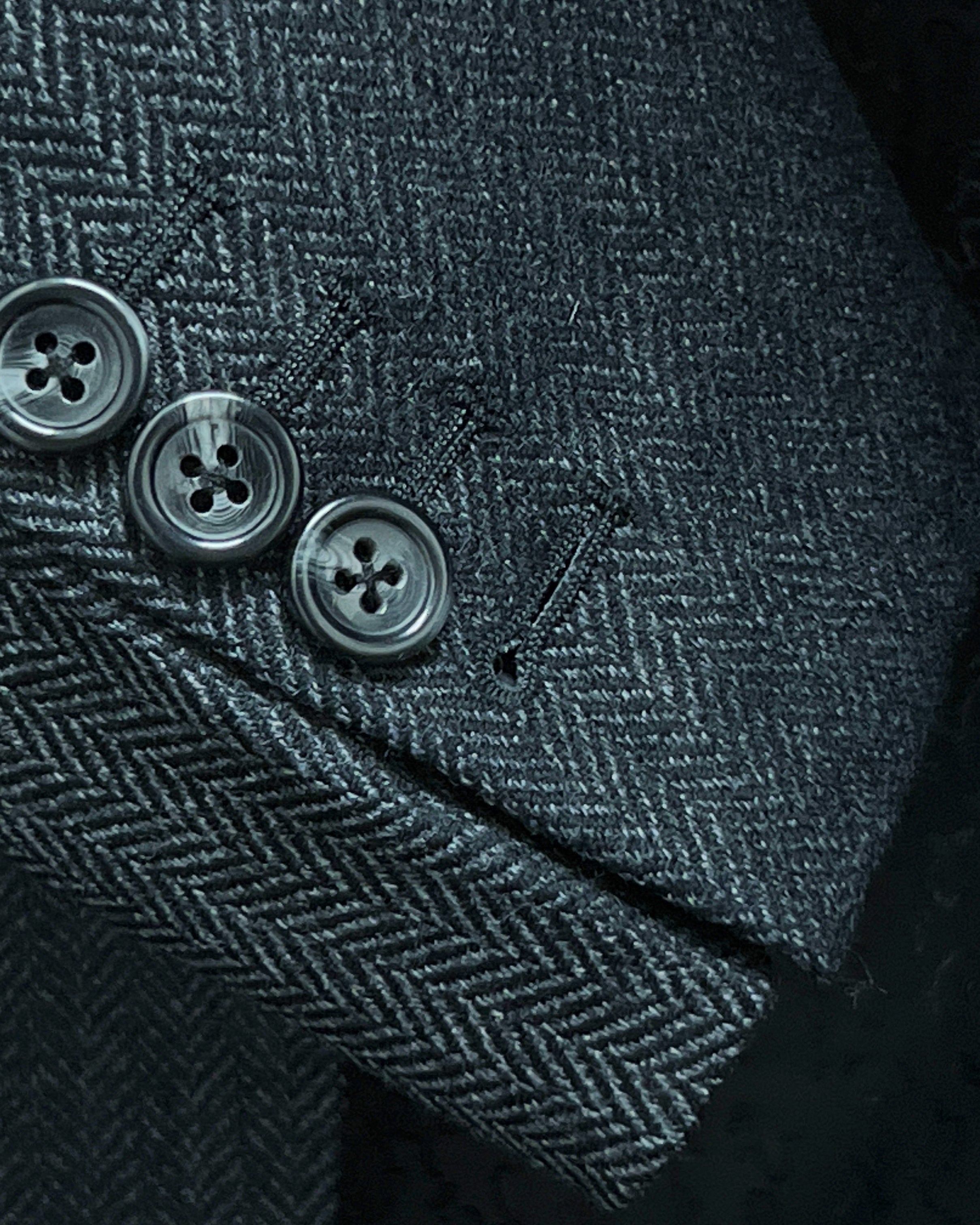 Sport coat sleeve cuff showing functional buttonholes with edge pick stitching on charcoal grey herringbone fabric