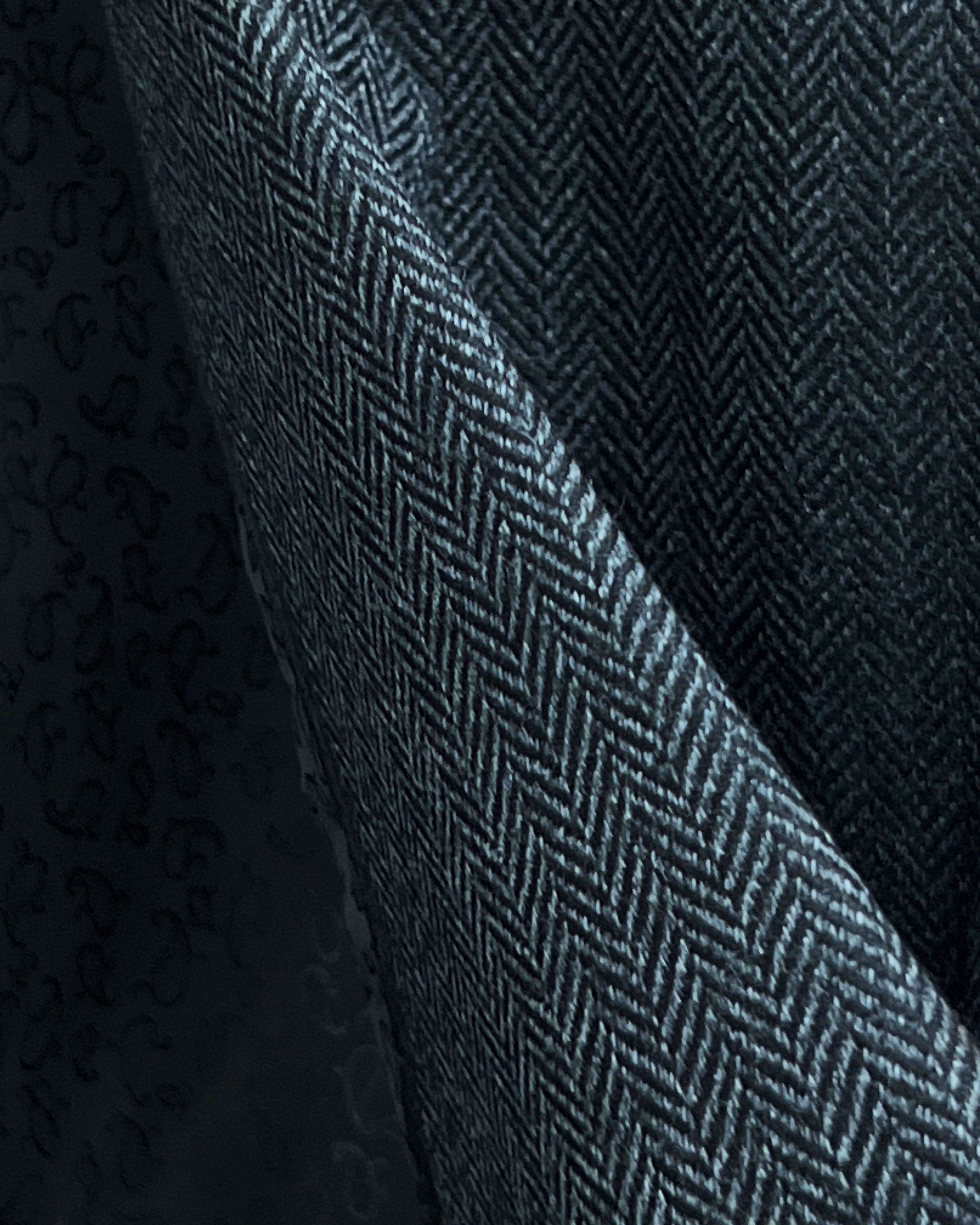 Close-up of charcoal grey herringbone tweed wool fabric showing distinctive diagonal weave pattern and texture