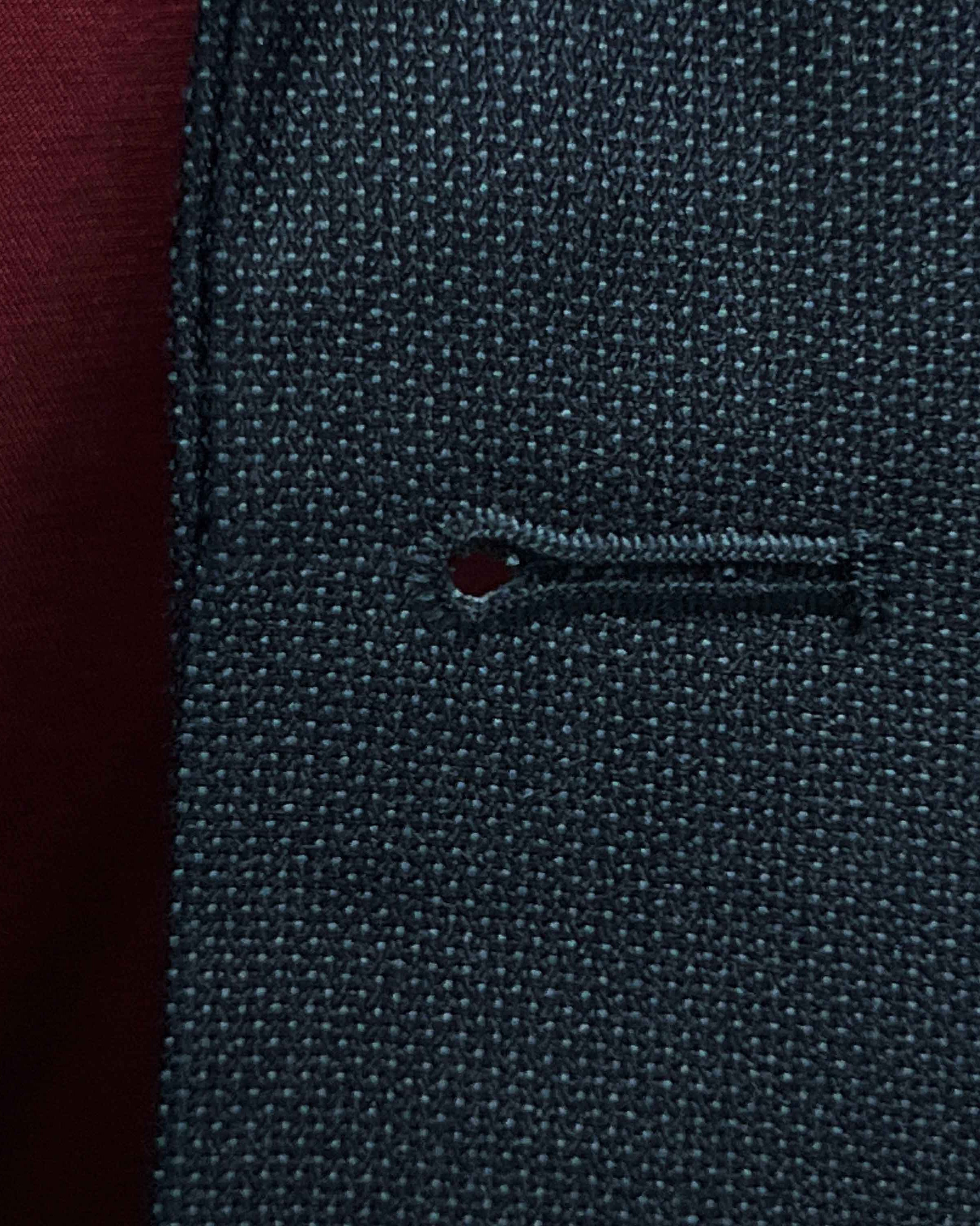 Detailed macro shot of hand-finished buttonhole stitching on dark charcoal grey birdseye suit with deep burgundy contrast thread