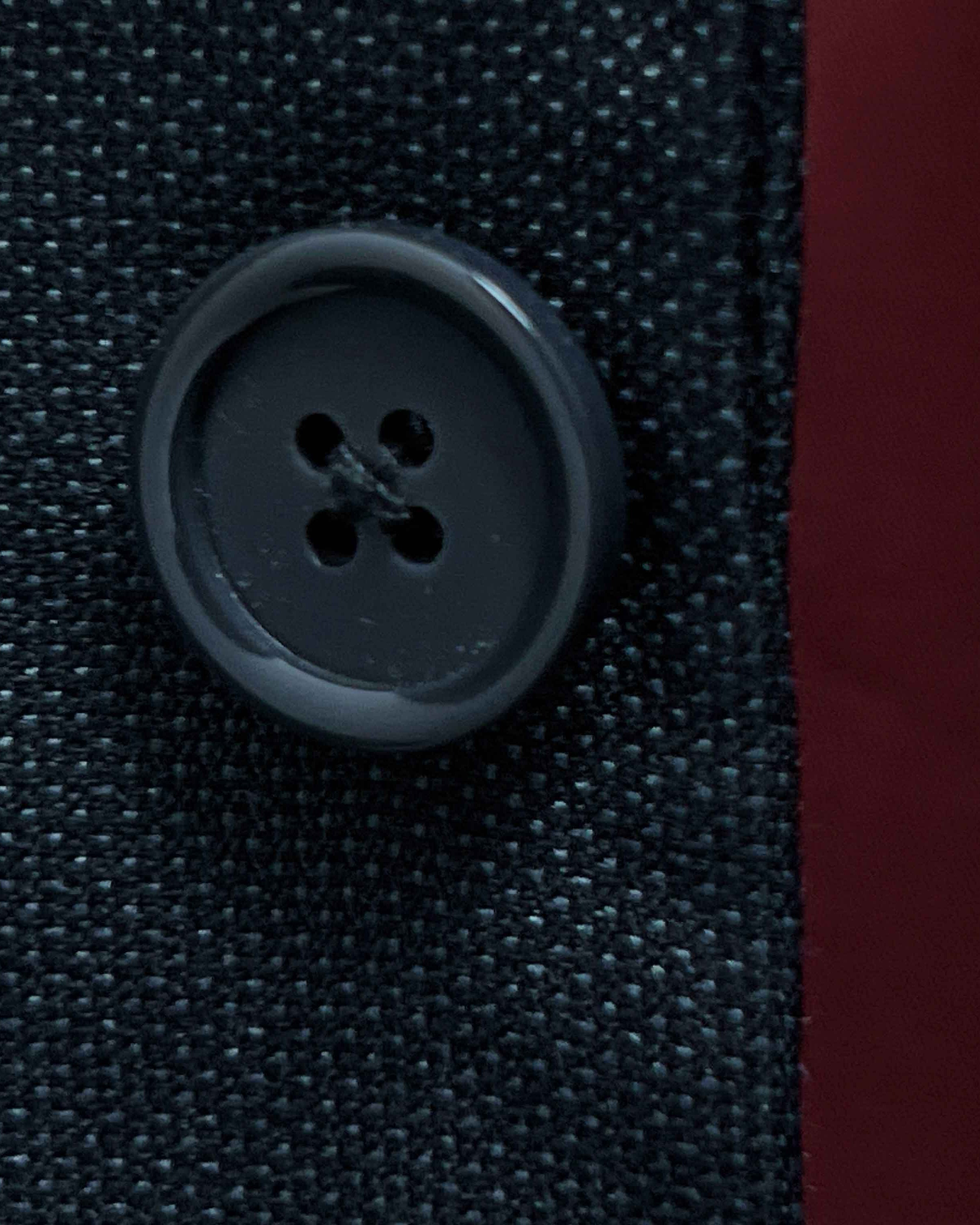 Close-up of dark grey horn buttons on dark charcoal grey birdseye suit jacket showing natural marble-like patterns