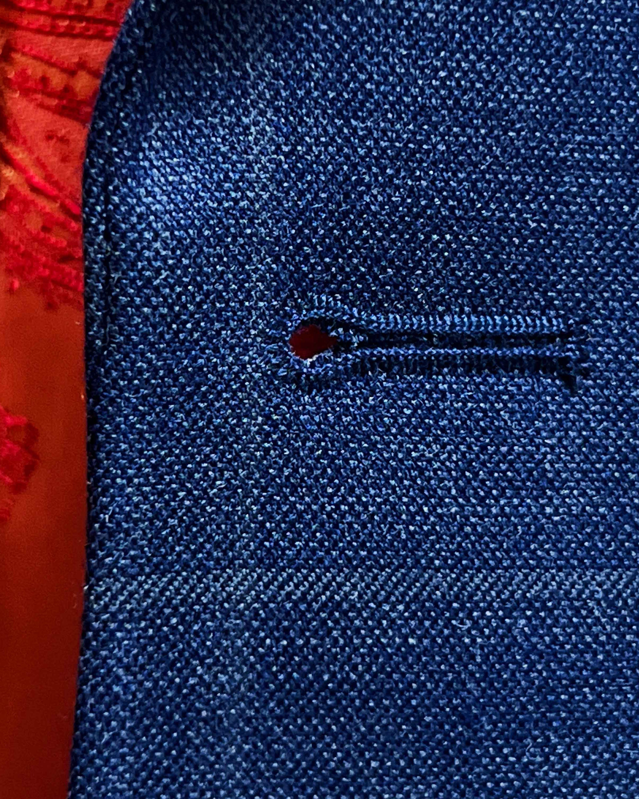 Detailed macro shot of hand-finished buttonhole stitching on deep blue windowpane check suit with orange contrast thread