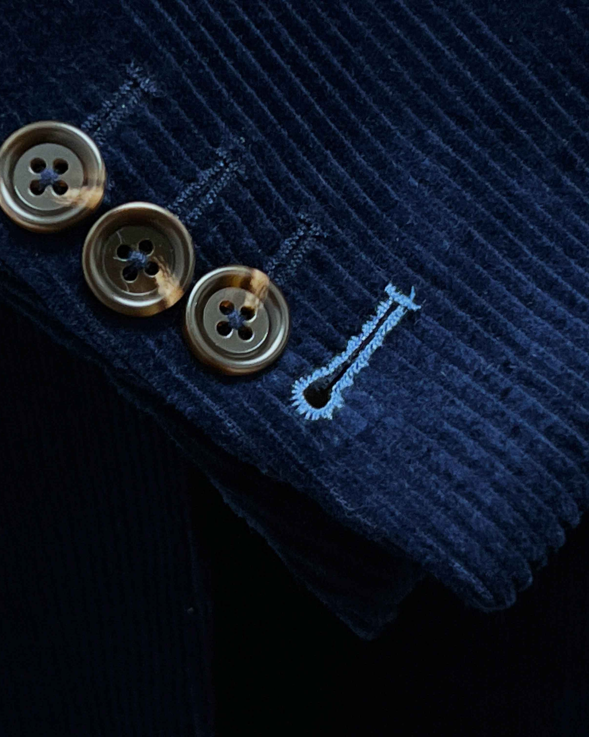 Sport coat sleeve cuff showing functional buttonholes with contrast light blue accent stitching on deep navy blue corduroy fabric