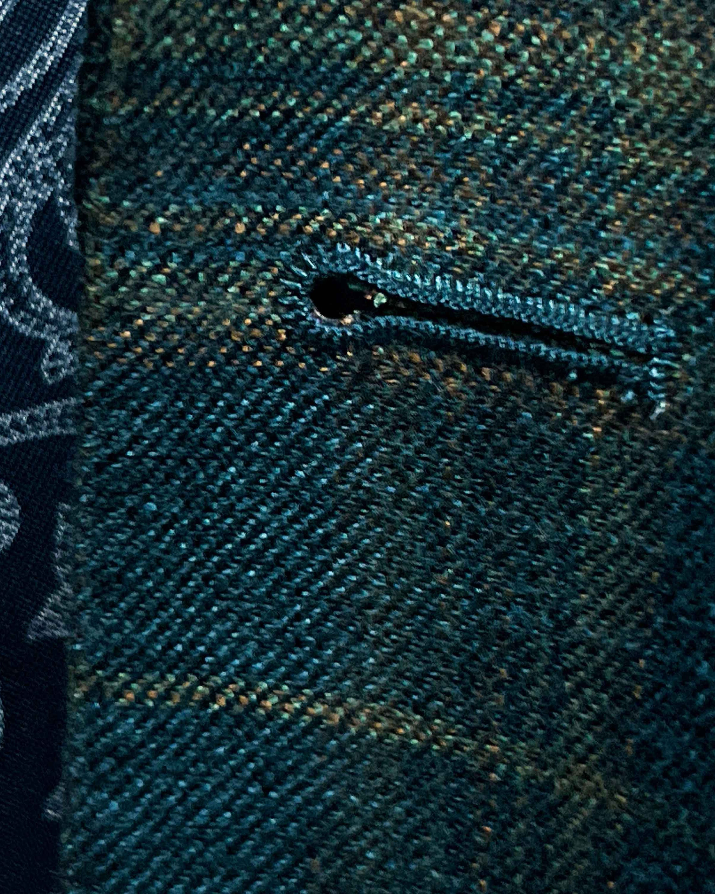 Detailed macro shot of hand-finished buttonhole stitching on deep teal green multi check suit with olive green contrast thread