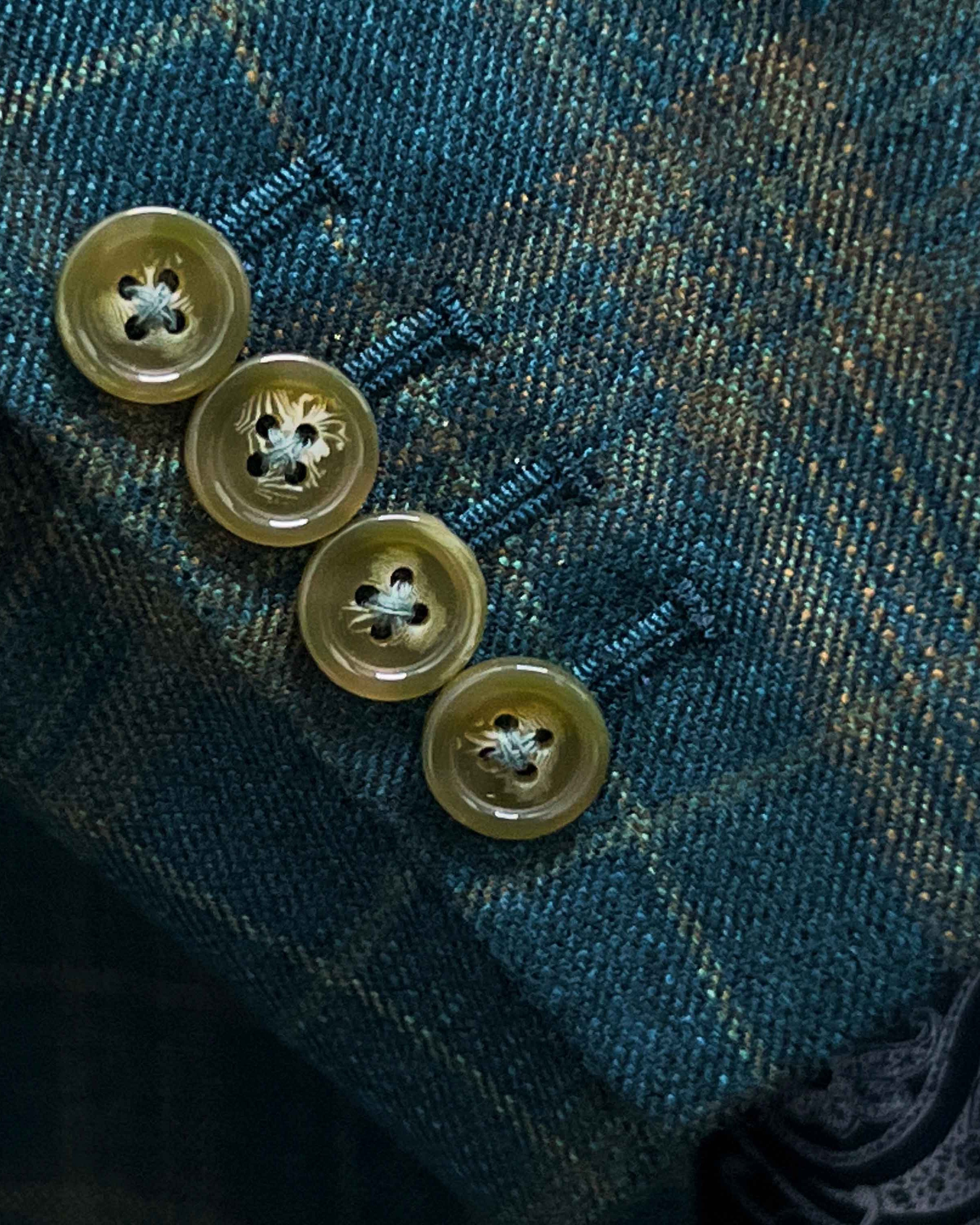 Suit jacket sleeve cuff showing functional buttonholes with contrast olive green accent stitching on deep teal green multi check fabric