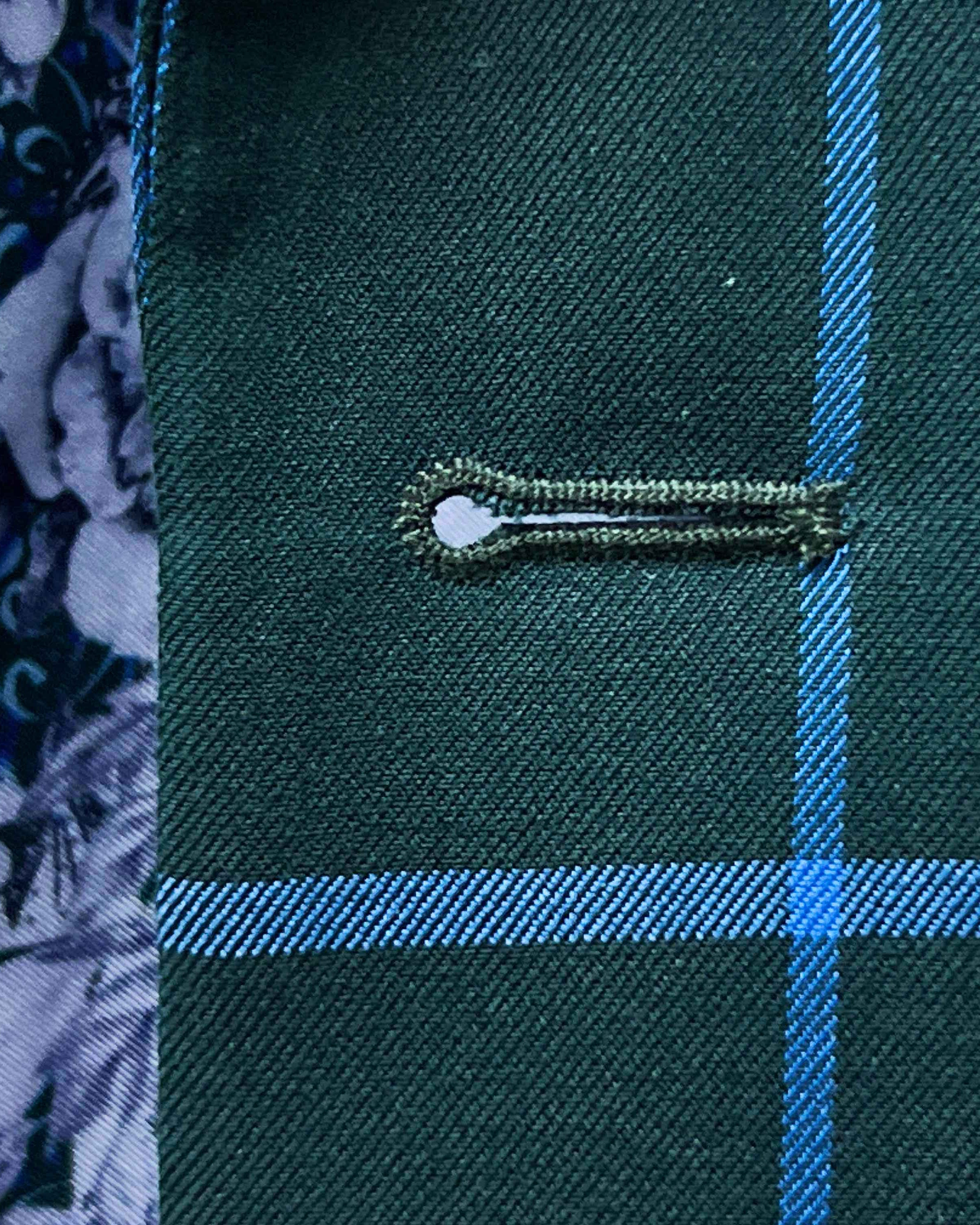 Detailed macro shot of hand-finished buttonhole stitching on forest green windowpane sport coat with bright blue contrast thread