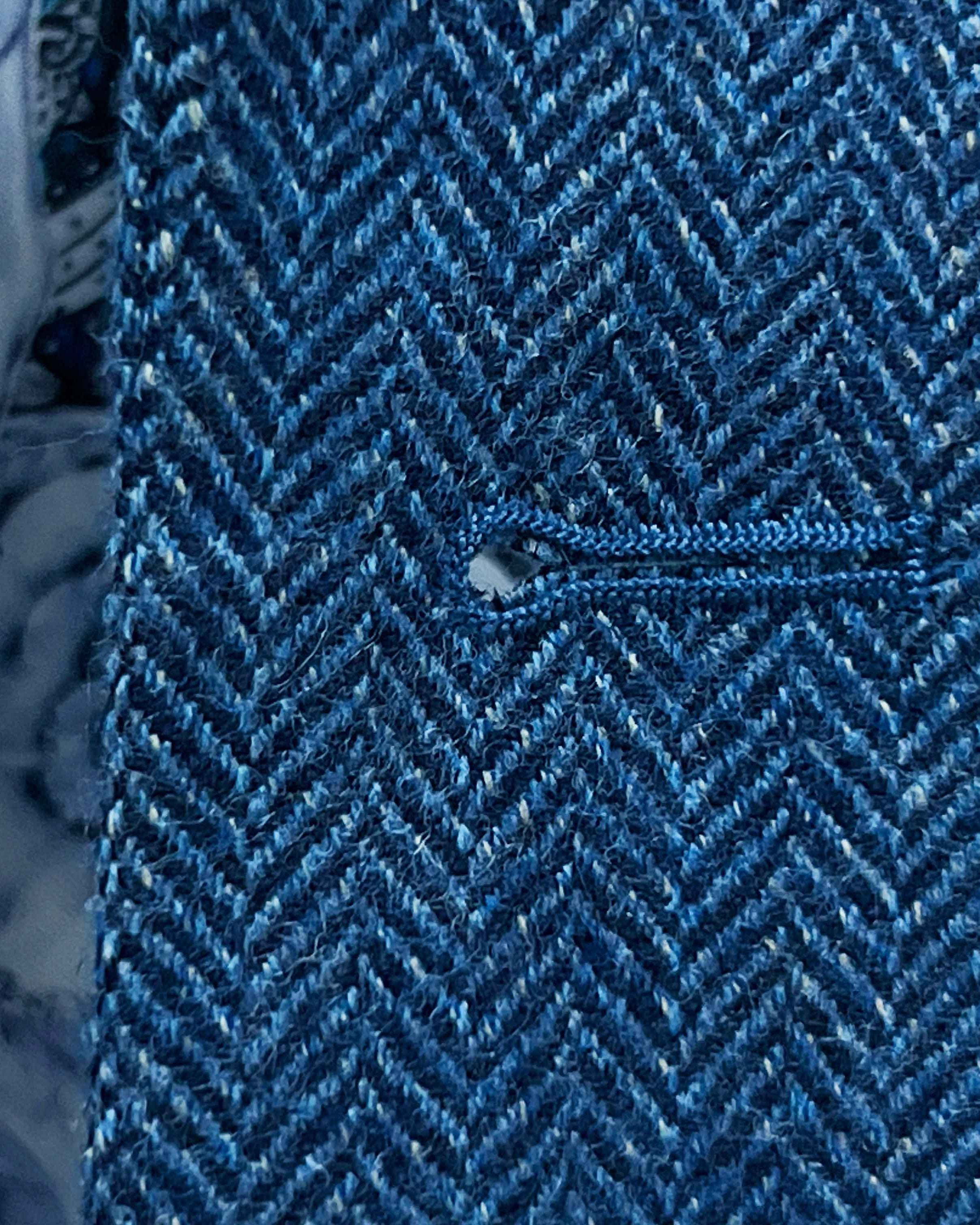 Detailed macro shot of hand-finished buttonhole stitching on indigo blue herringbone tweed sport coat with royal blue contrast thread