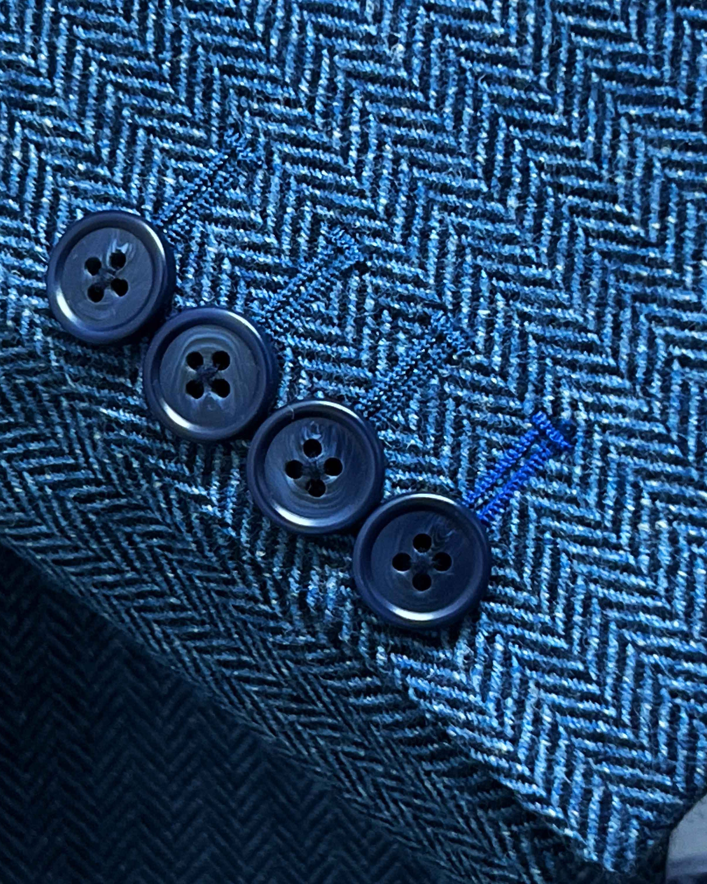 Sport coat sleeve cuff showing functional buttonholes with contrast royal blue accent stitching on indigo blue herringbone tweed fabric