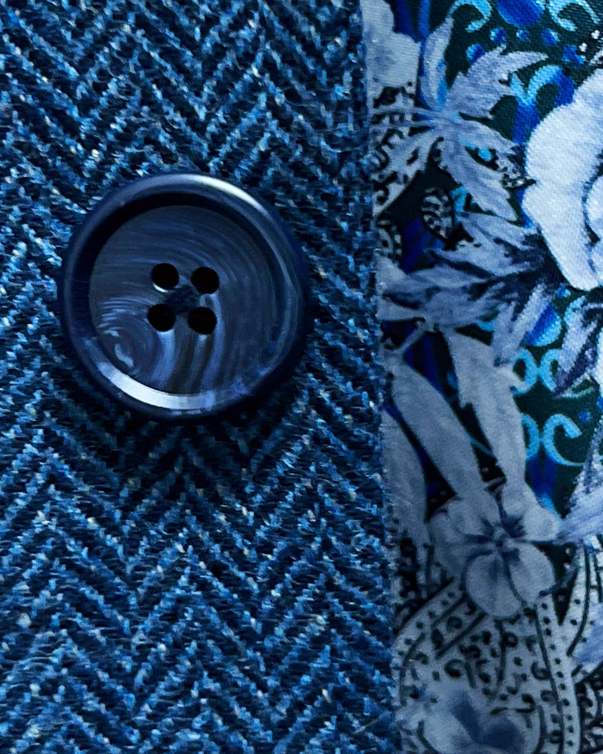 Close-up of a blue textured fabric with a button and floral embroidery.