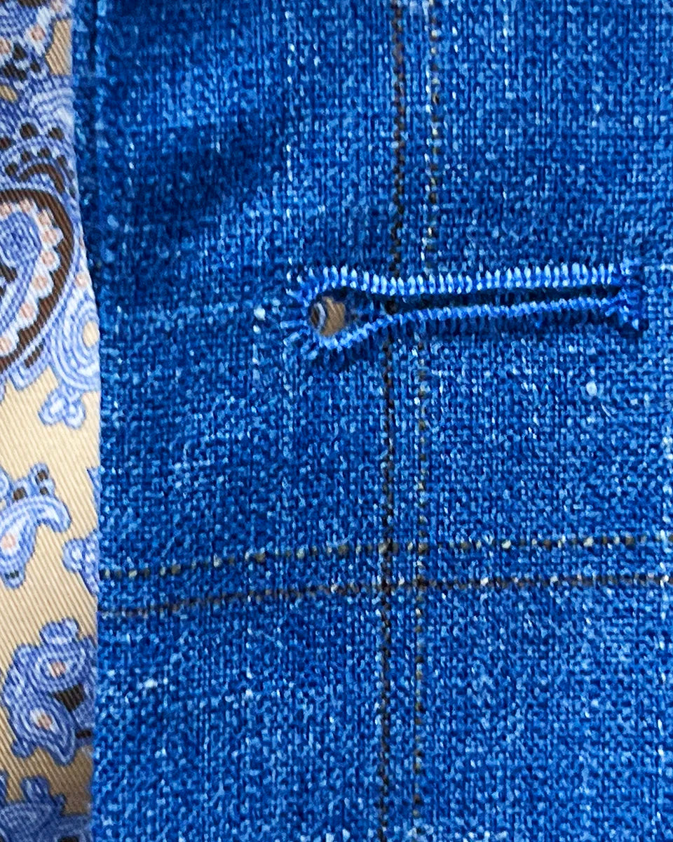 Macro view of precision buttonhole stitching showing chocolate brown thread contrast against light blue windowpane weave