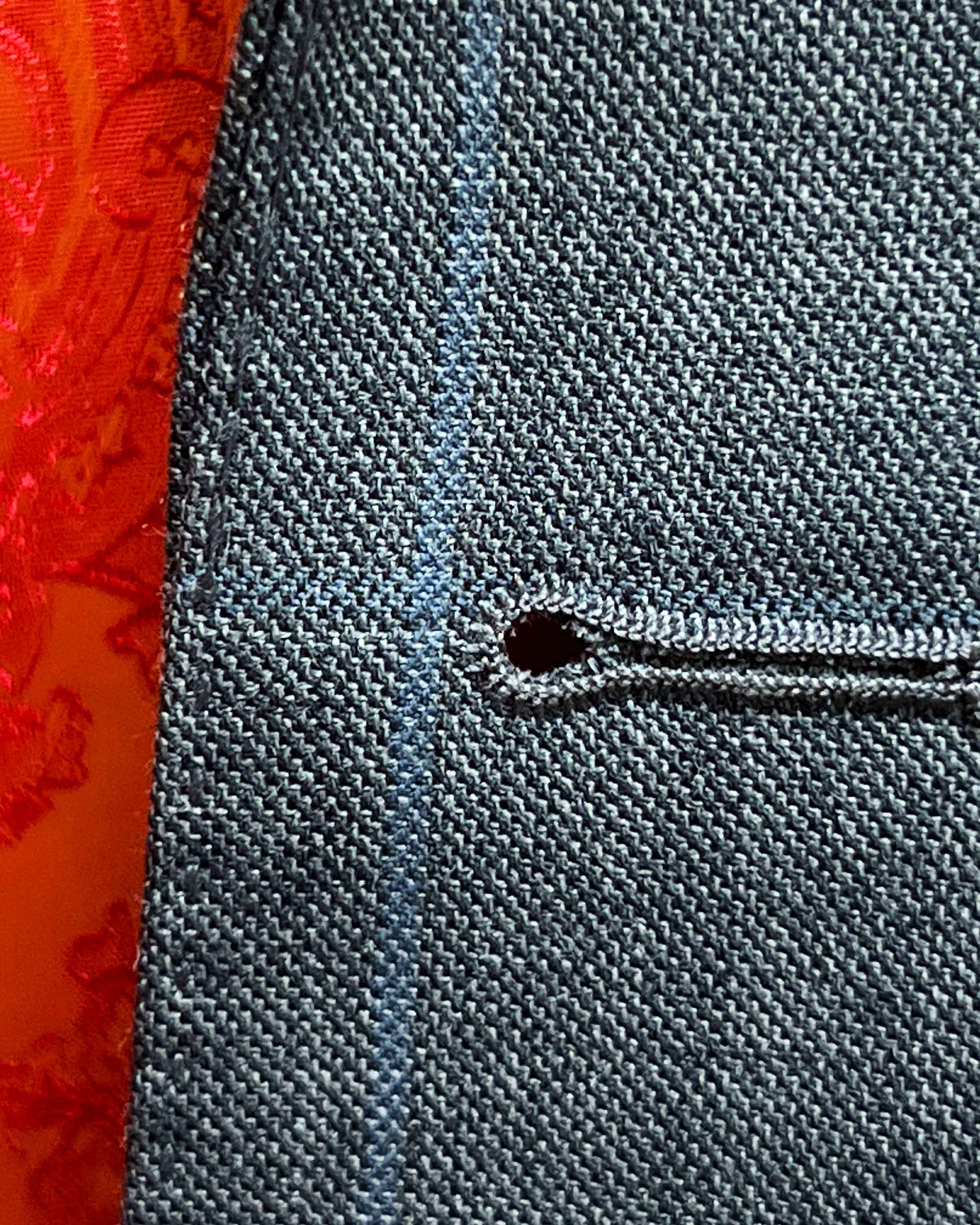 Detailed macro shot of hand-finished buttonhole stitching on light gray with light blue windowpane sport coat with bright orange contrast thread
