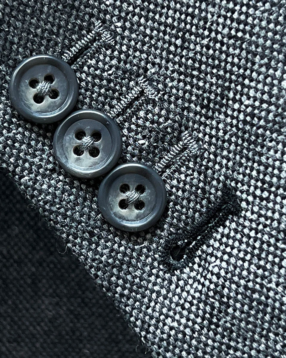 Close-up of working sleeve buttons with black contrast buttonholes and pick stitching on light grey tweed