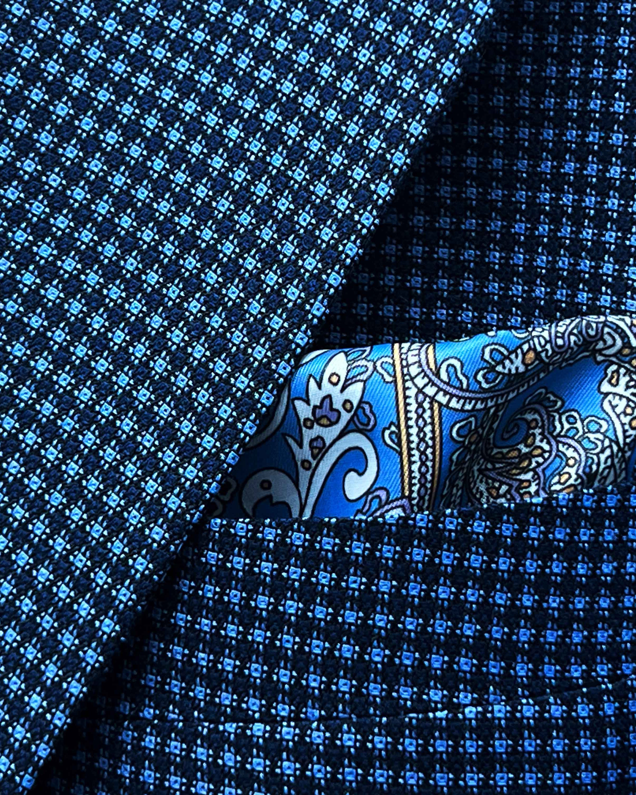 Breast pocket of medium blue micro check sport coat with matching paisley pocket square and hand-finished edges