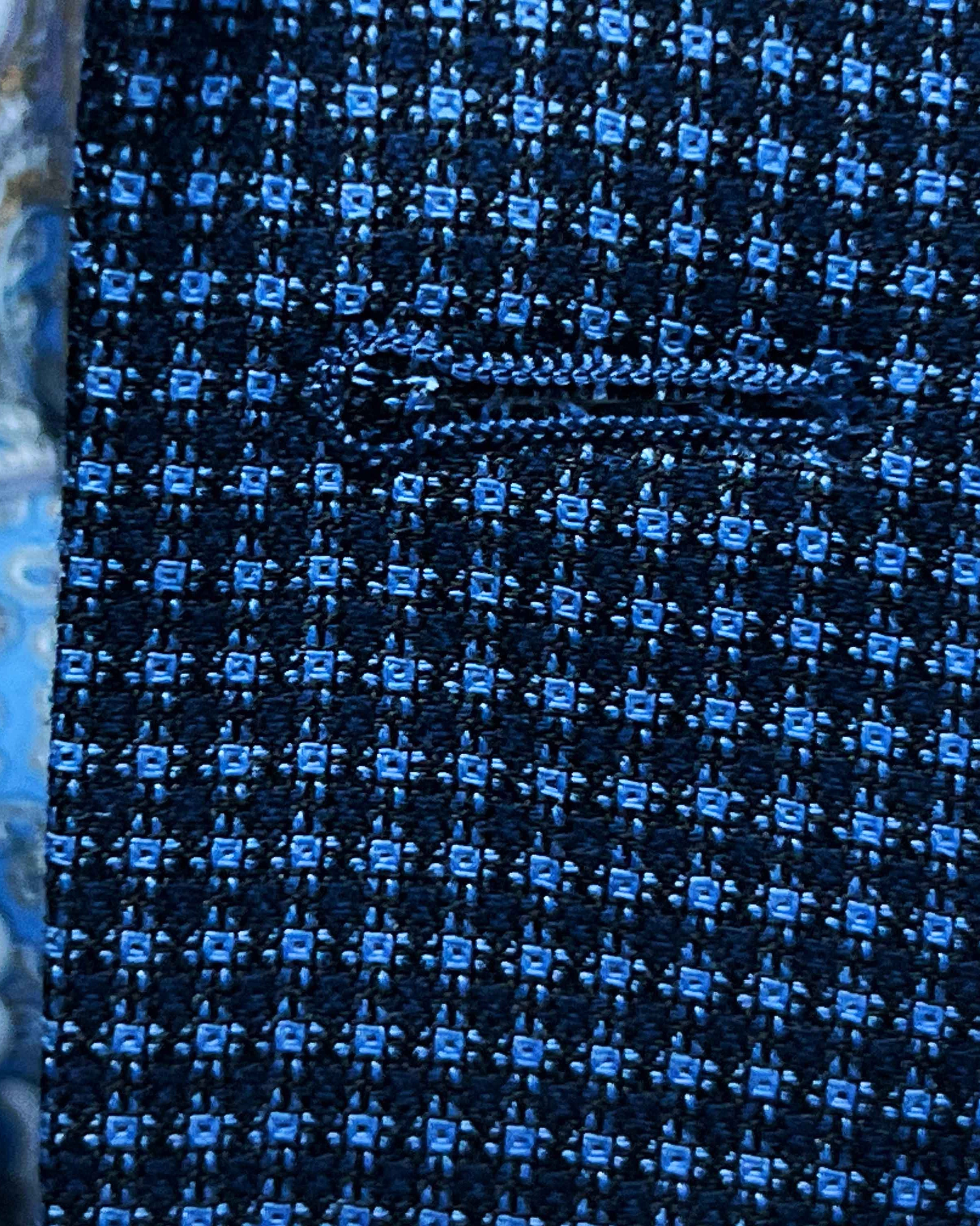 Detailed macro shot of hand-finished buttonhole stitching on medium blue micro check sport coat with light blue contrast thread