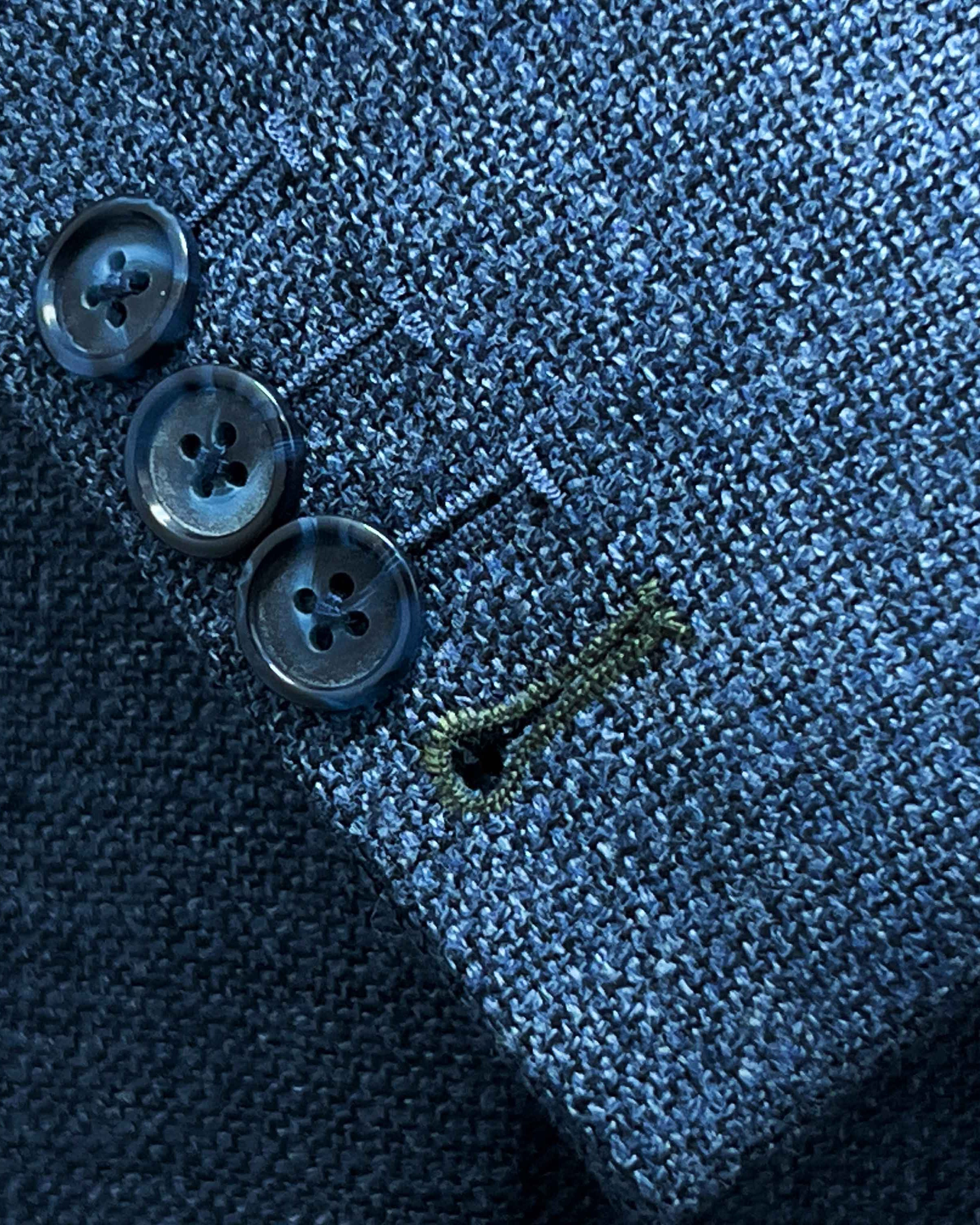 Sport coat sleeve cuff showing functional buttonholes with olive green contrast accent stitching on medium steel blue hopsack fabric