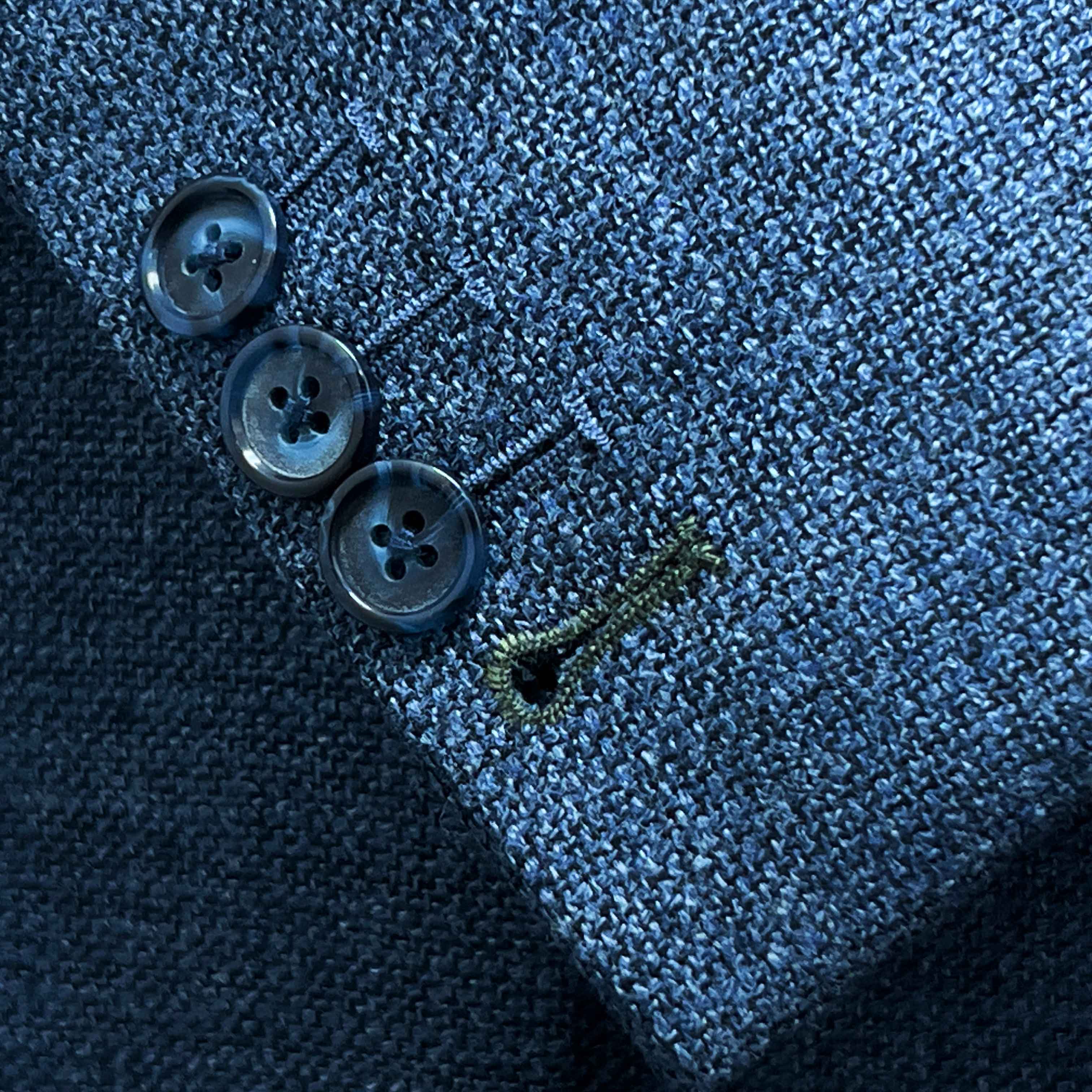 Sport coat sleeve cuff showing functional buttonholes with olive green contrast accent stitching on medium steel blue hopsack fabric