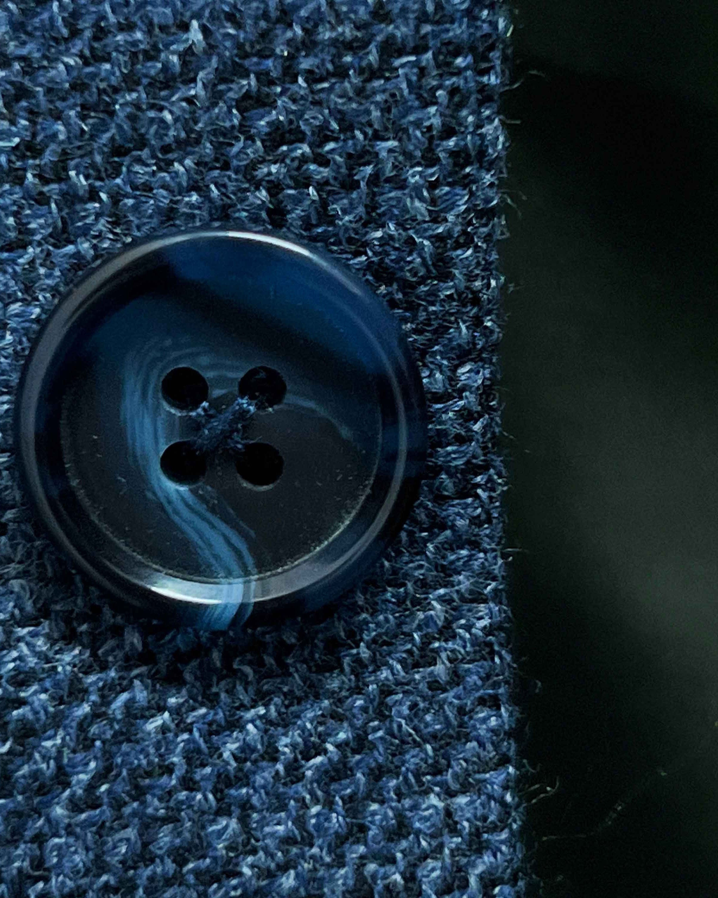 Close-up of dark navy horn buttons with light blue marbling on medium steel blue hopsack sport coat showing natural patterns