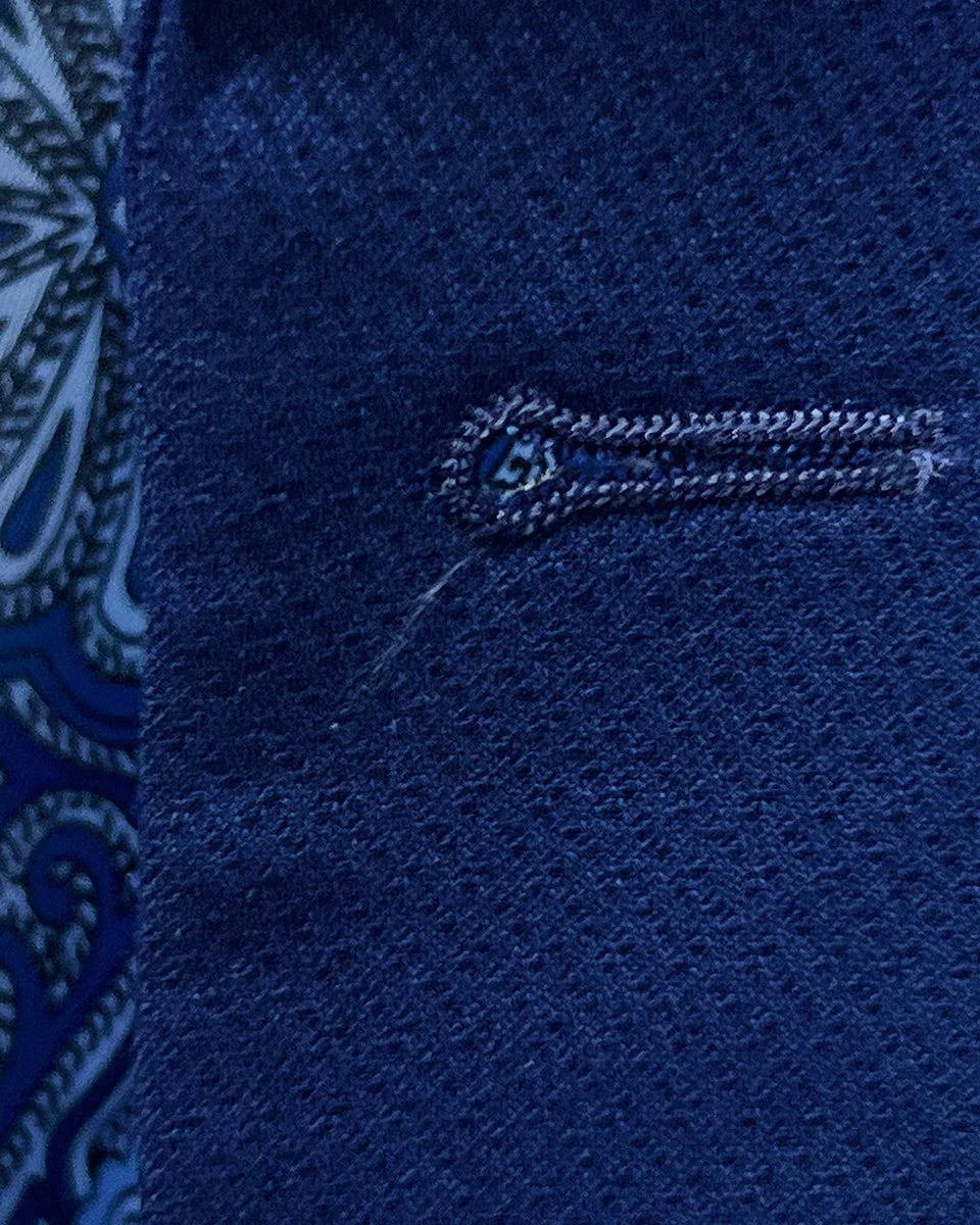 Detailed macro shot of hand-finished buttonhole stitching on navy blue geometric textured suit with light blue contrast thread