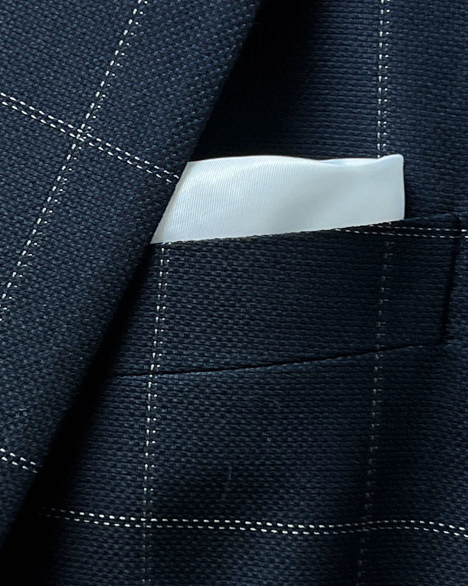 Close-up of white silk bemberg built-in pocket square in navy windowpane suit jacket breast pocket