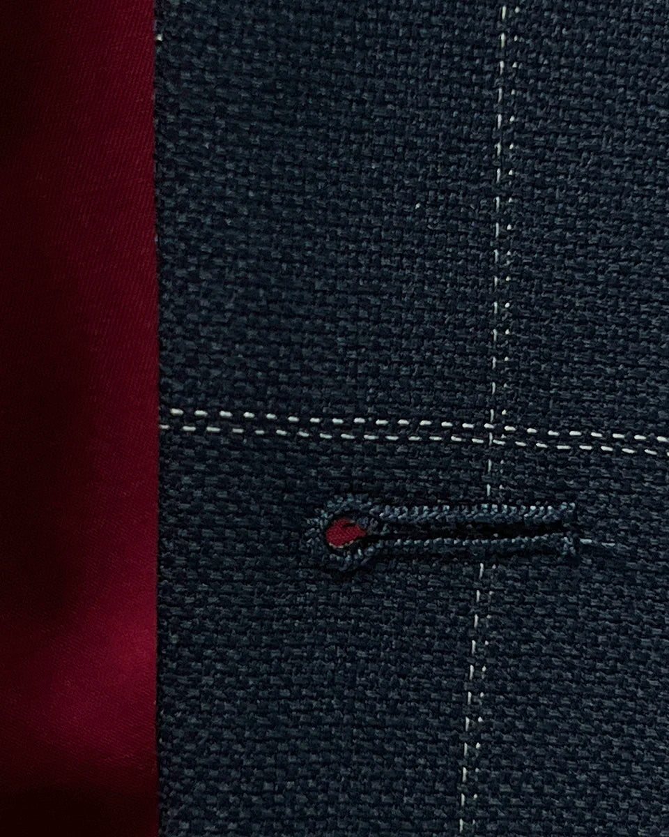 Macro view of buttonhole stitching on navy windowpane suit jacket, demonstrating quality craftsmanship