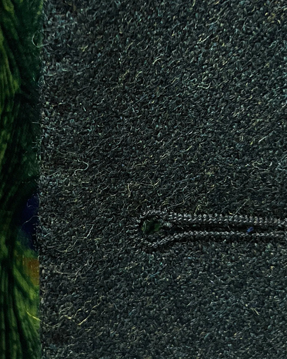 Detailed view of black contrast buttonhole stitching showing precise handwork on olive tweed fabric