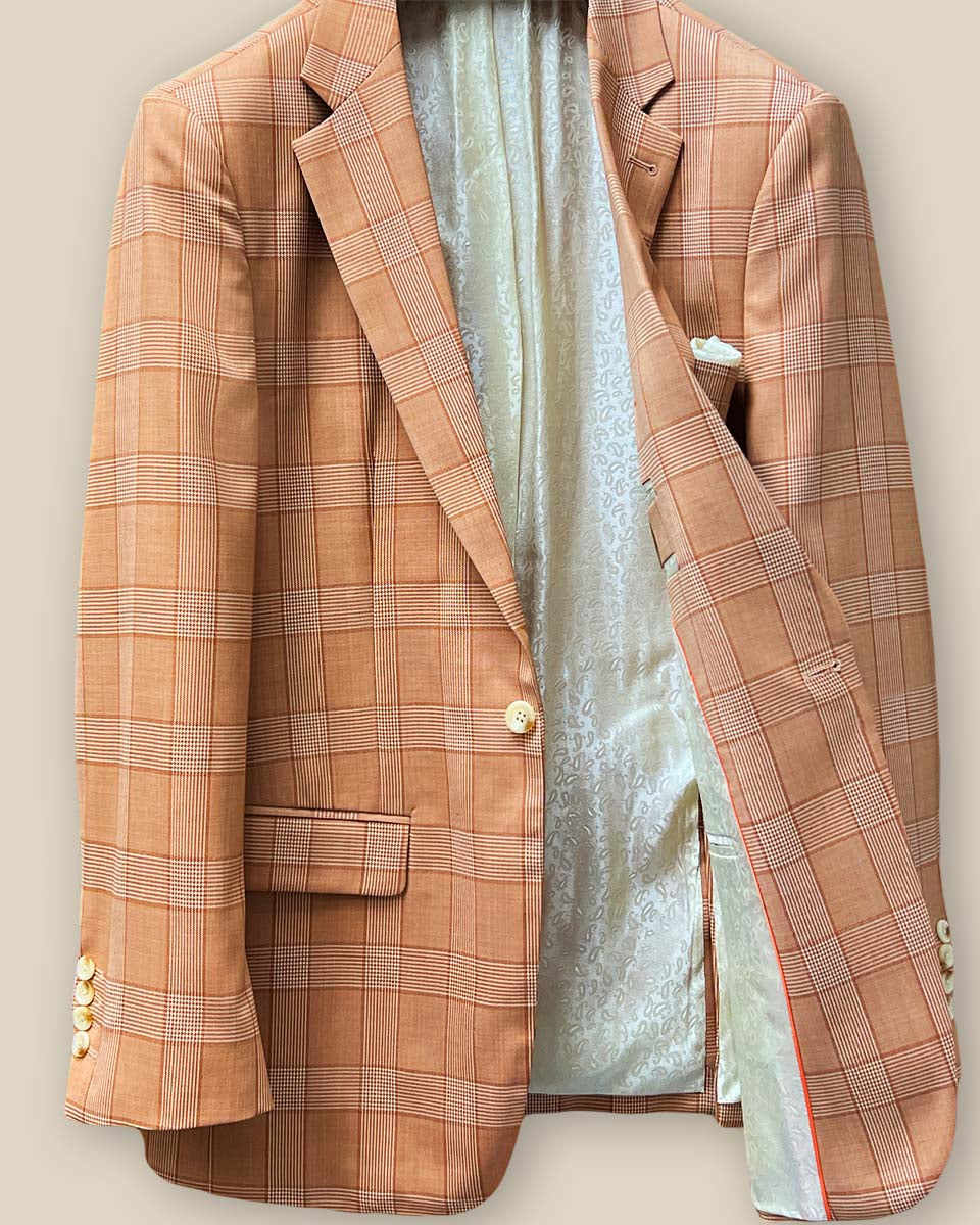 Interior view of orange suit jacket's left side, showcasing ivory paisley flash lining and bright orange piping