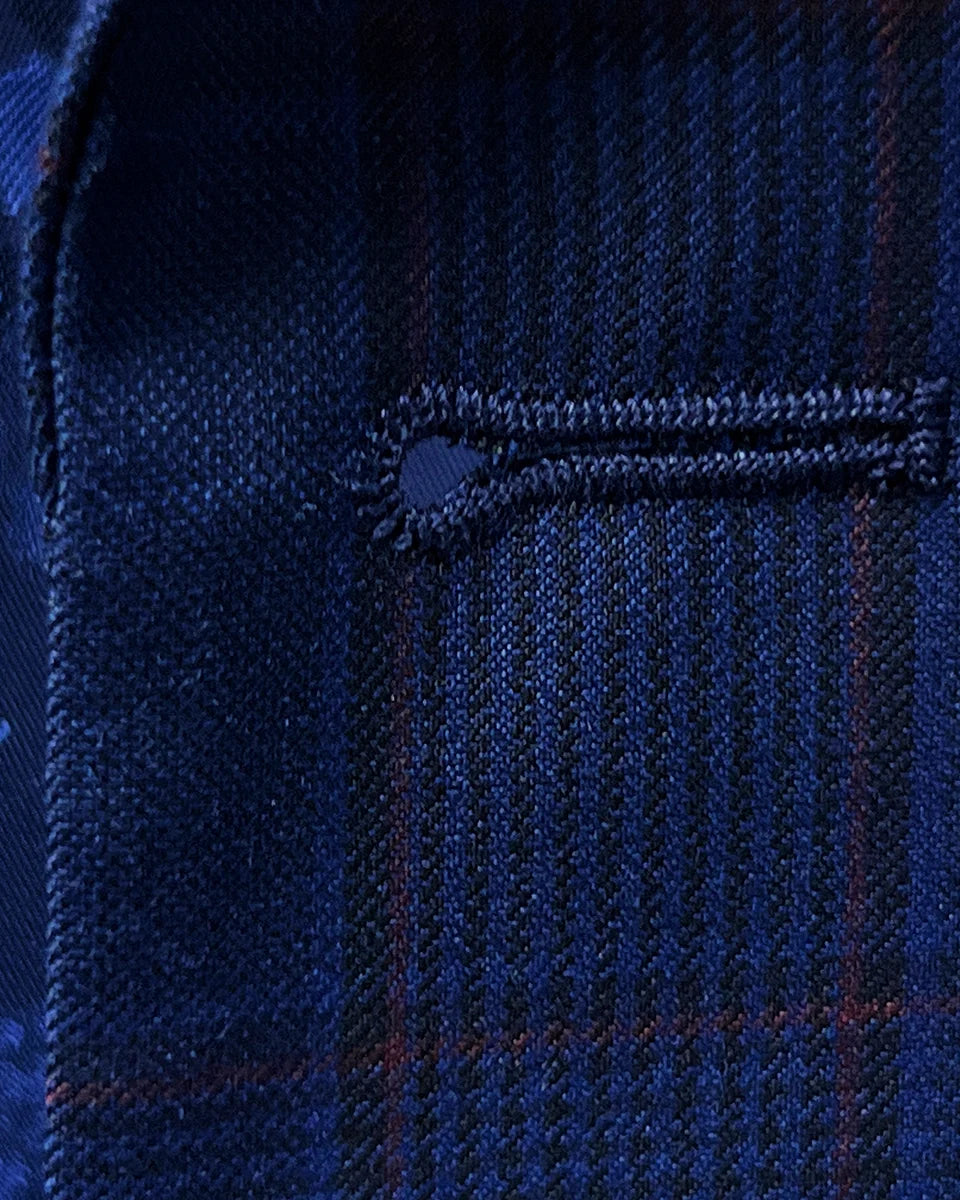 Macro detail of precision buttonhole stitching showing crimson red accent thread work against royal blue plaid background