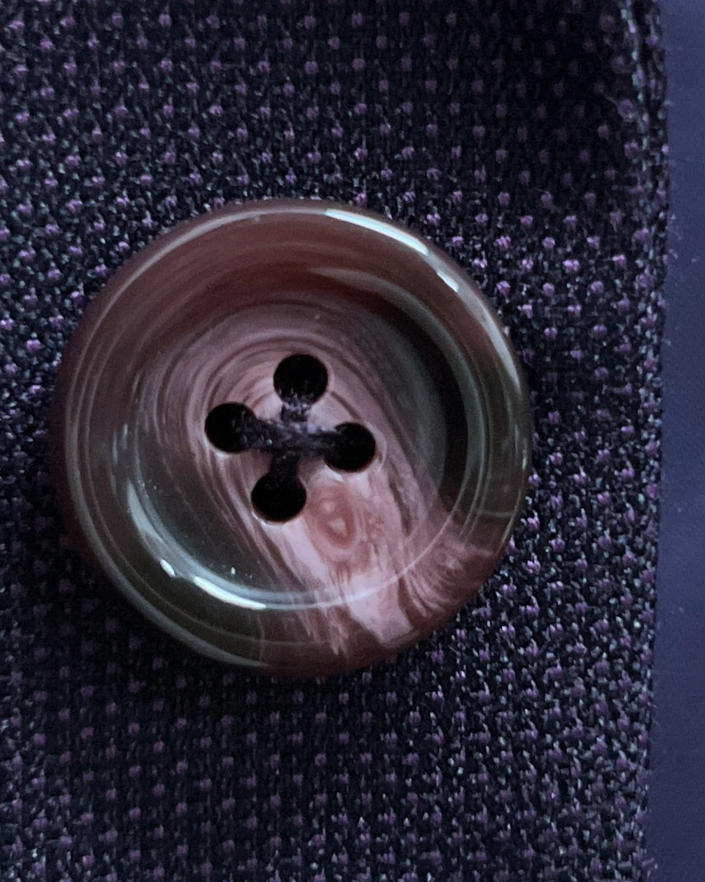 Button macro of aubergine birdseye men's suit showing a burgundy horn button.