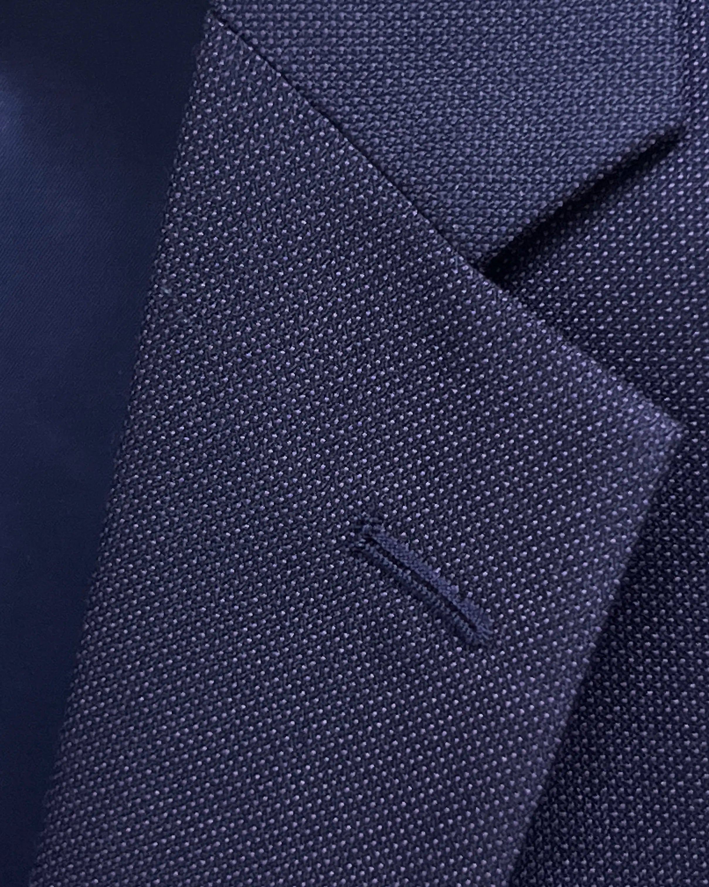 Lapel buttonhole close up of aubergine birdseye men's suit showing standard matching stitching.