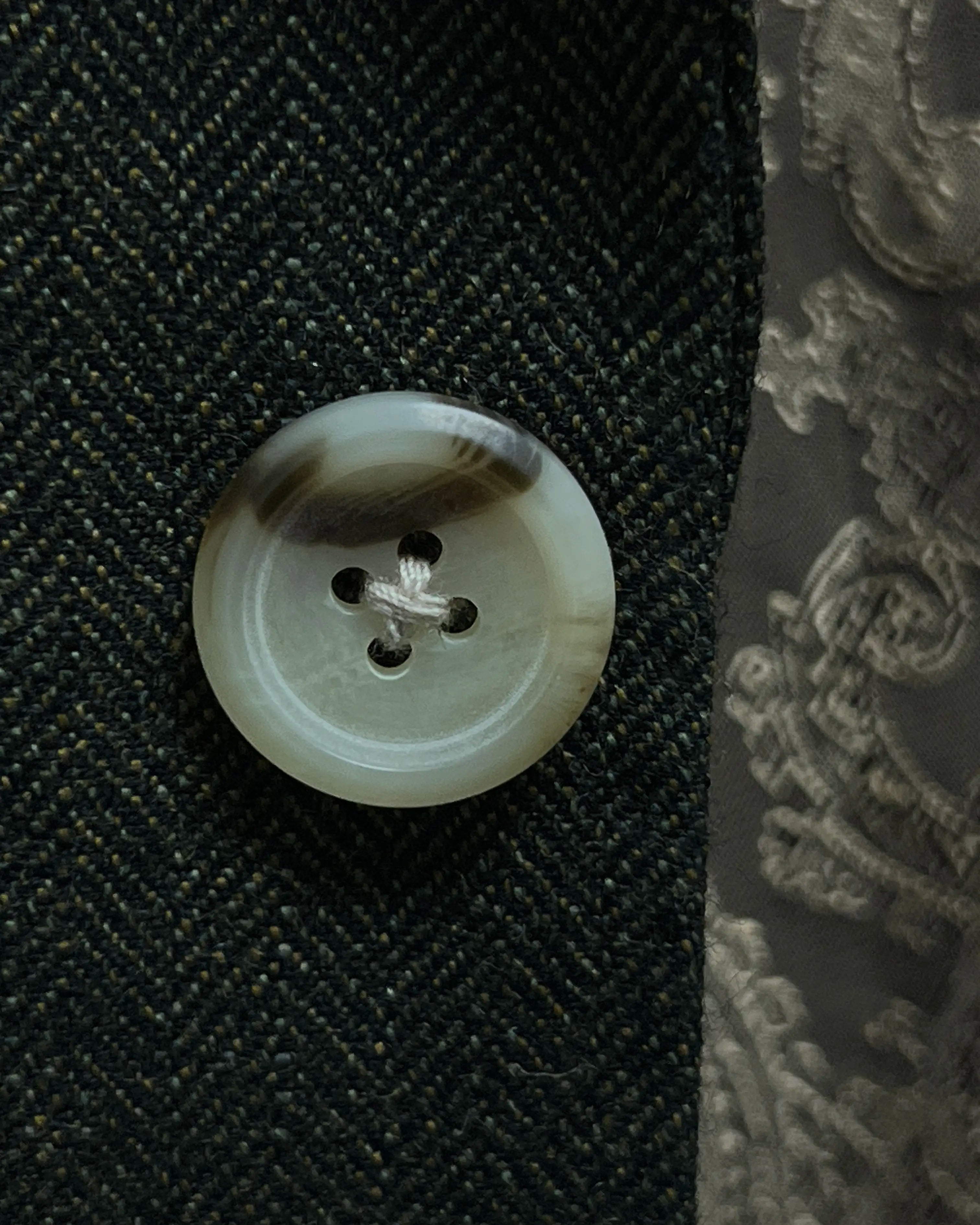 Button close up of dark forest green herringbone men's suit showing eggshell horn buttons