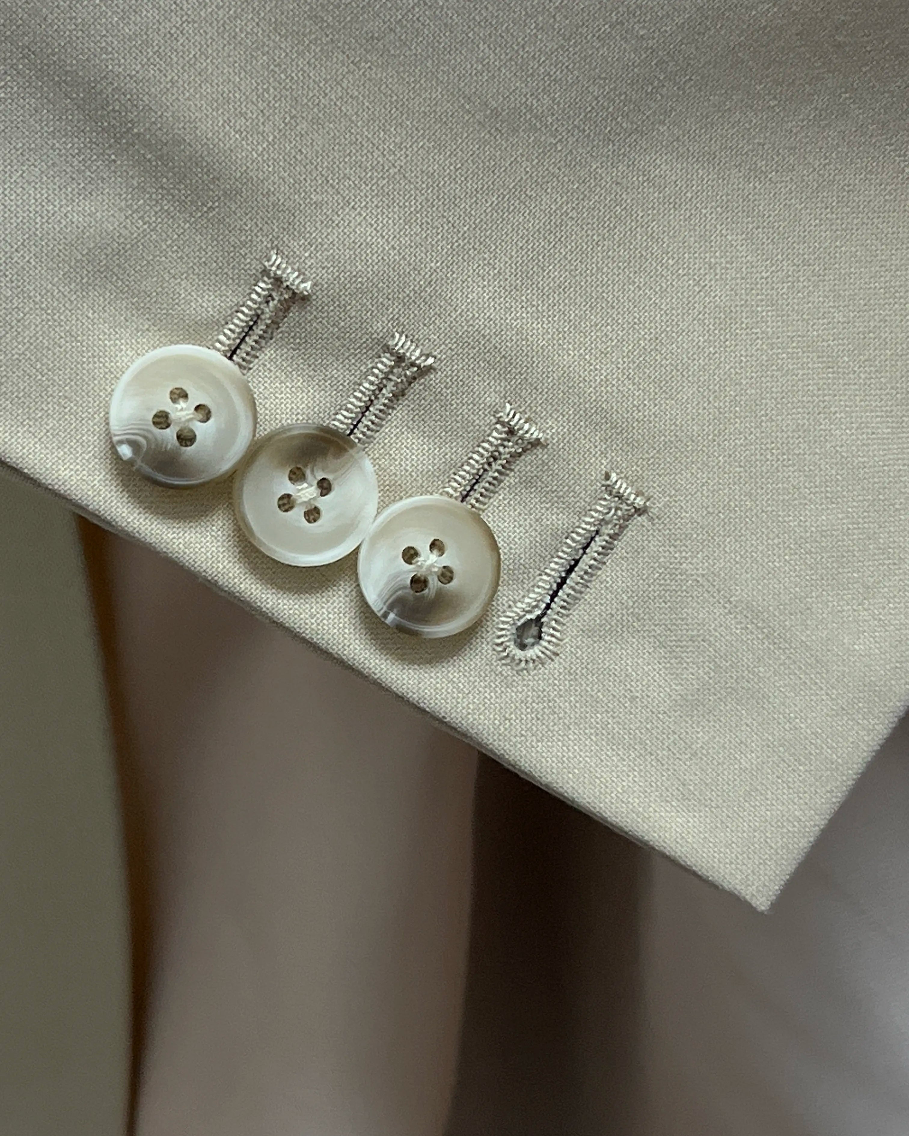 Sleeve cuff close up of light beige plain men's suit showing functional sleeve buttons