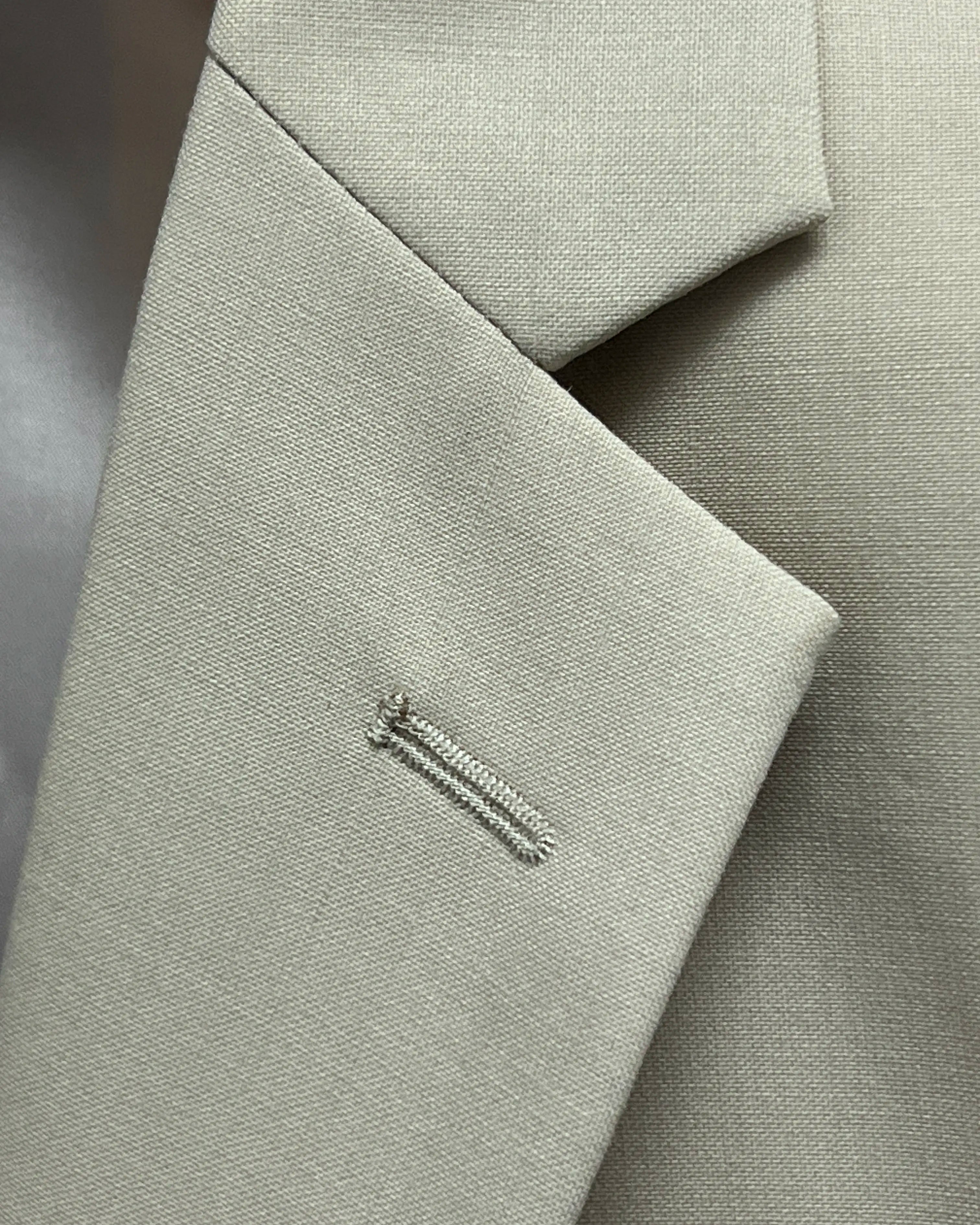 Lapel buttonhole close up of light beige plain men's suit showing standard lapel buttonhole stitching