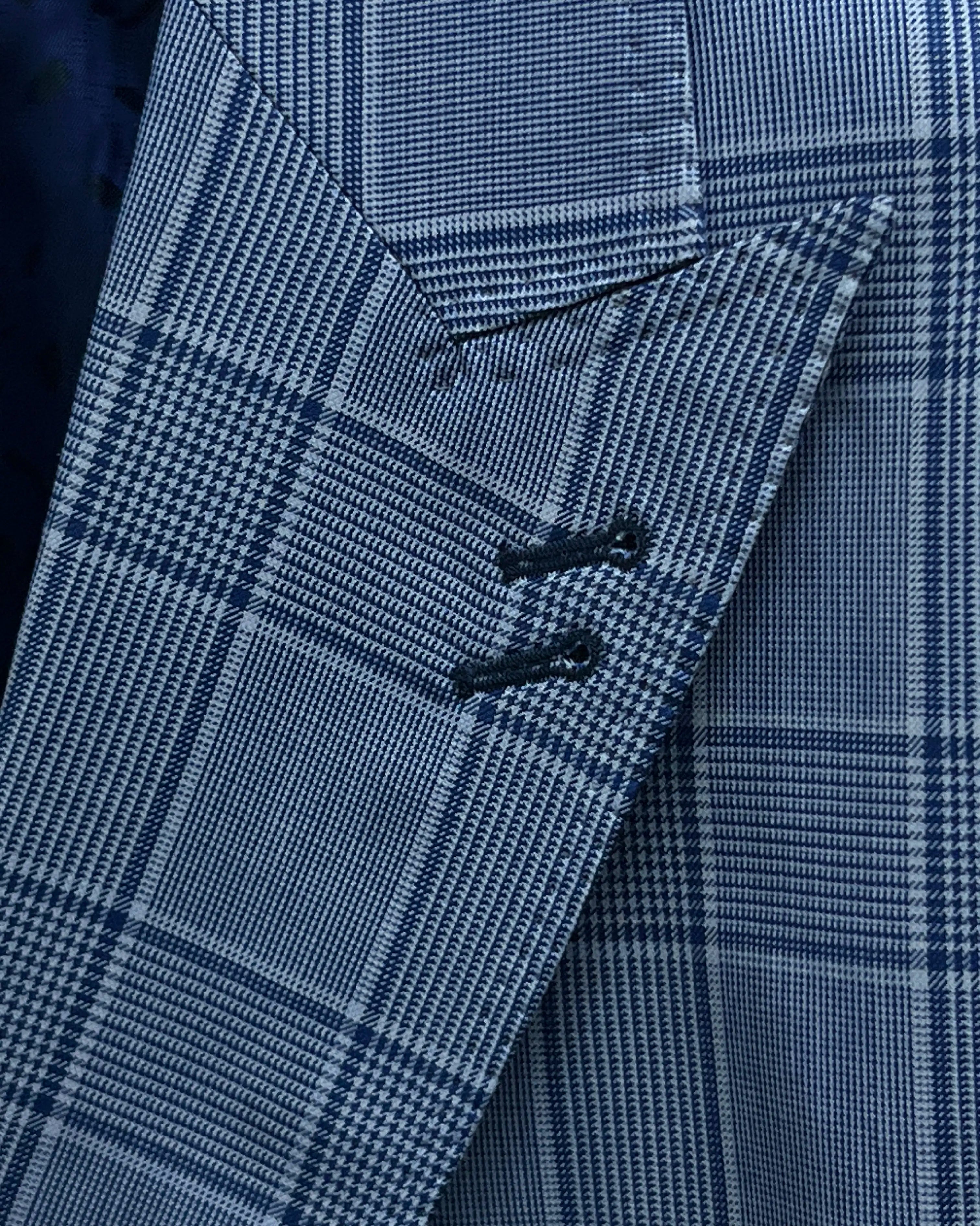 Lapel buttonhole close up of light blue Prince of Wales glen plaid with navy windowpane men's suit showing double navy contrast lapel buttonholes