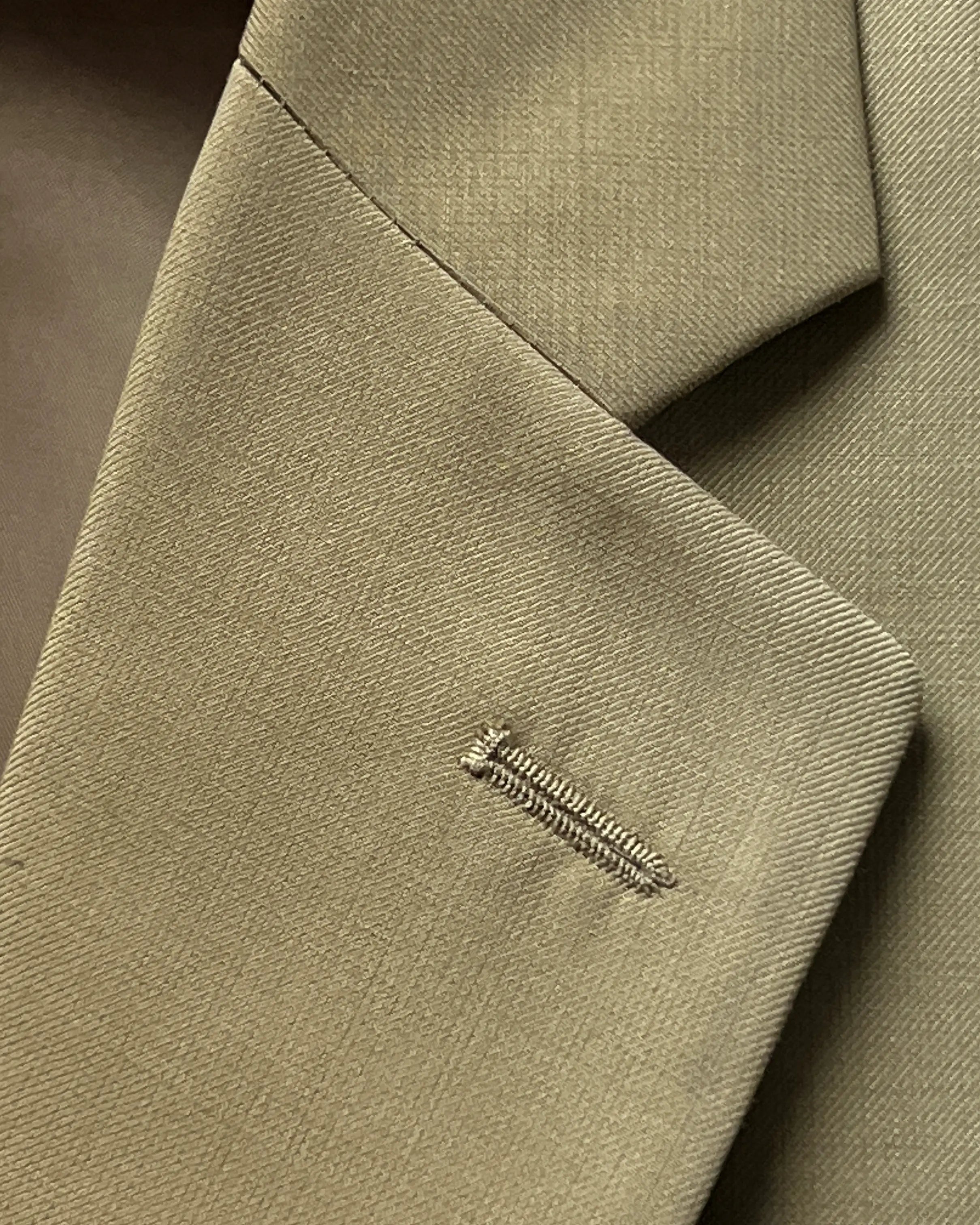 Lapel close up of brown plain men's suit showing matching lapel buttonhole detail