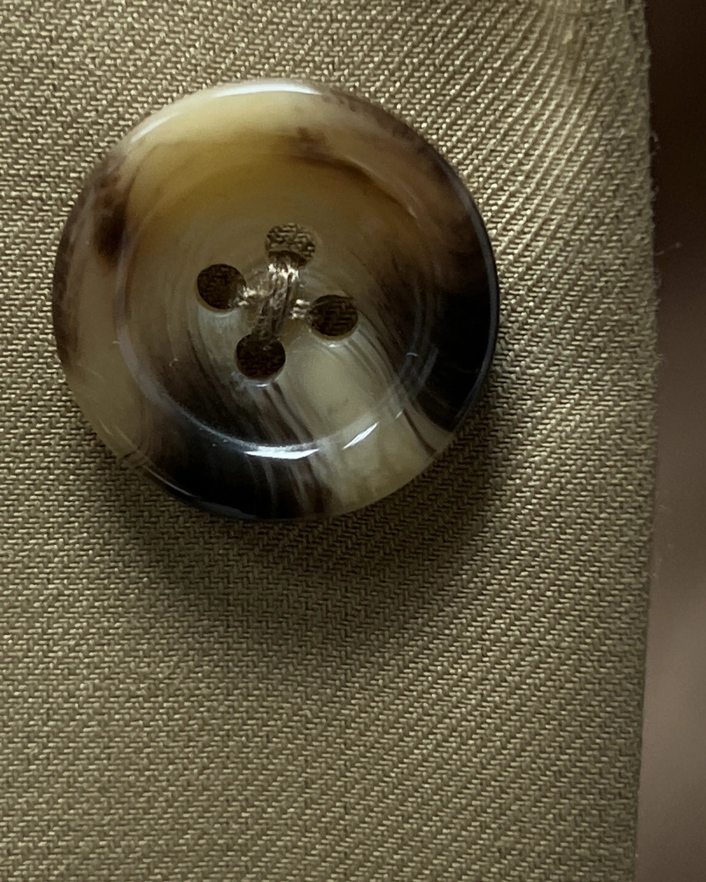 Button close up of brown plain men's suit showing mottled beige and dark brown horn buttons