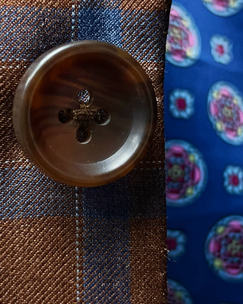 Close-up of natural brown horn buttons showing unique marble patterns and premium button craftsmanship against check fabric