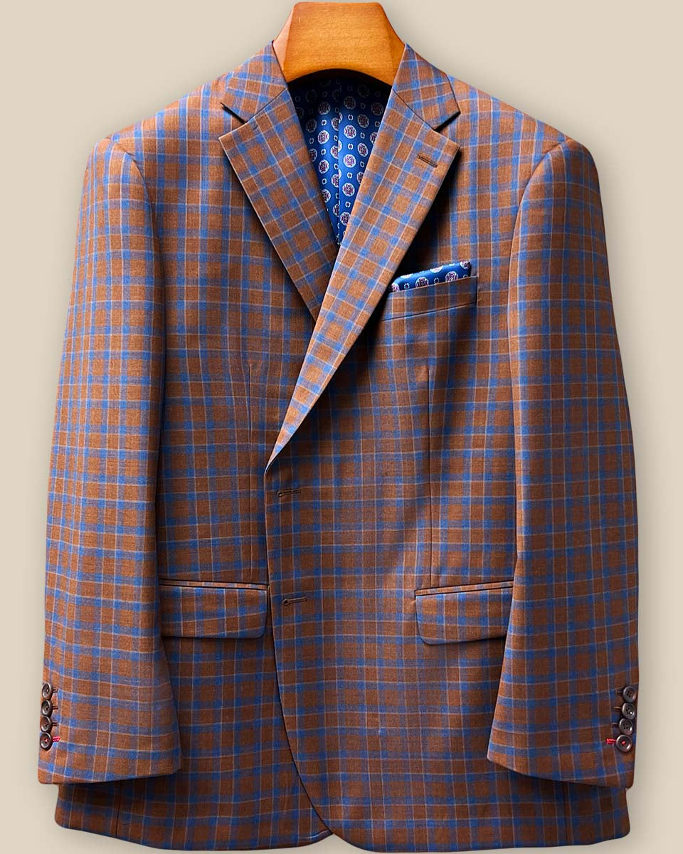 Close-up view of red contrast accent buttonholes on jacket sleeve showing precise hand-stitched detailing against tobacco brown and cobalt blue check pattern